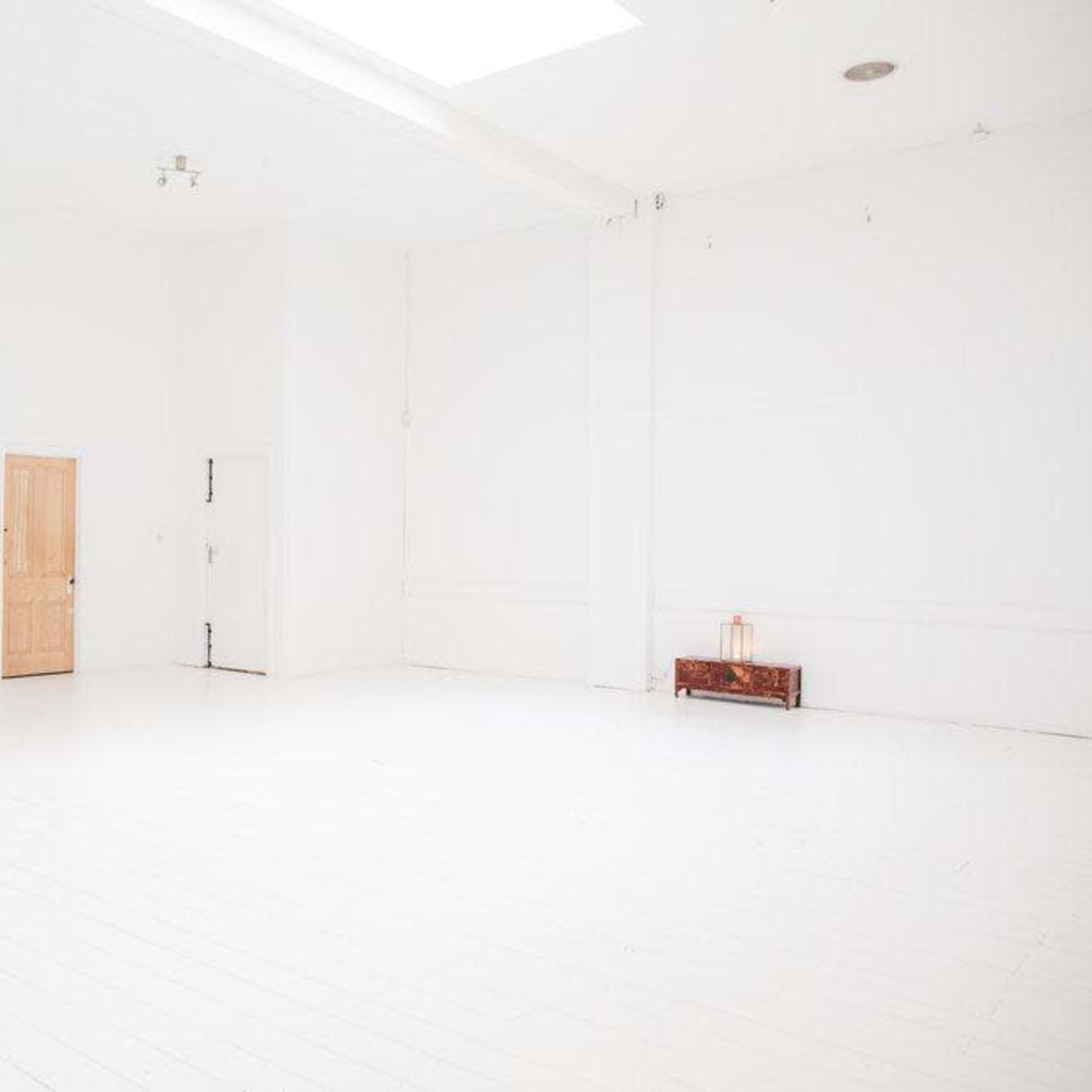 A spacious, empty white room with two doors and a small wooden bench against the wall.
