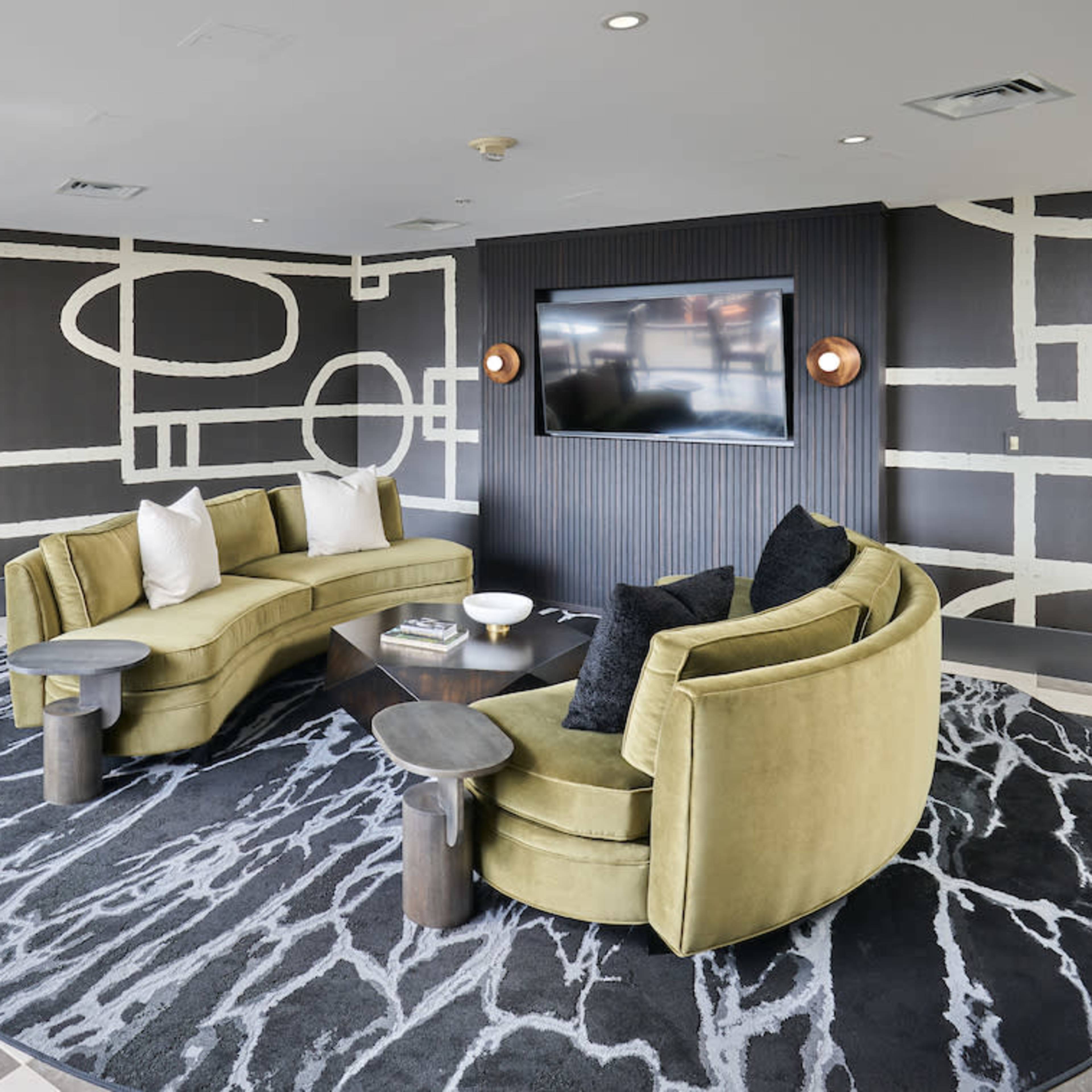 A modern lounge area featuring a curved green sofa, a round rug, a coffee table, and a large wall-mounted TV.