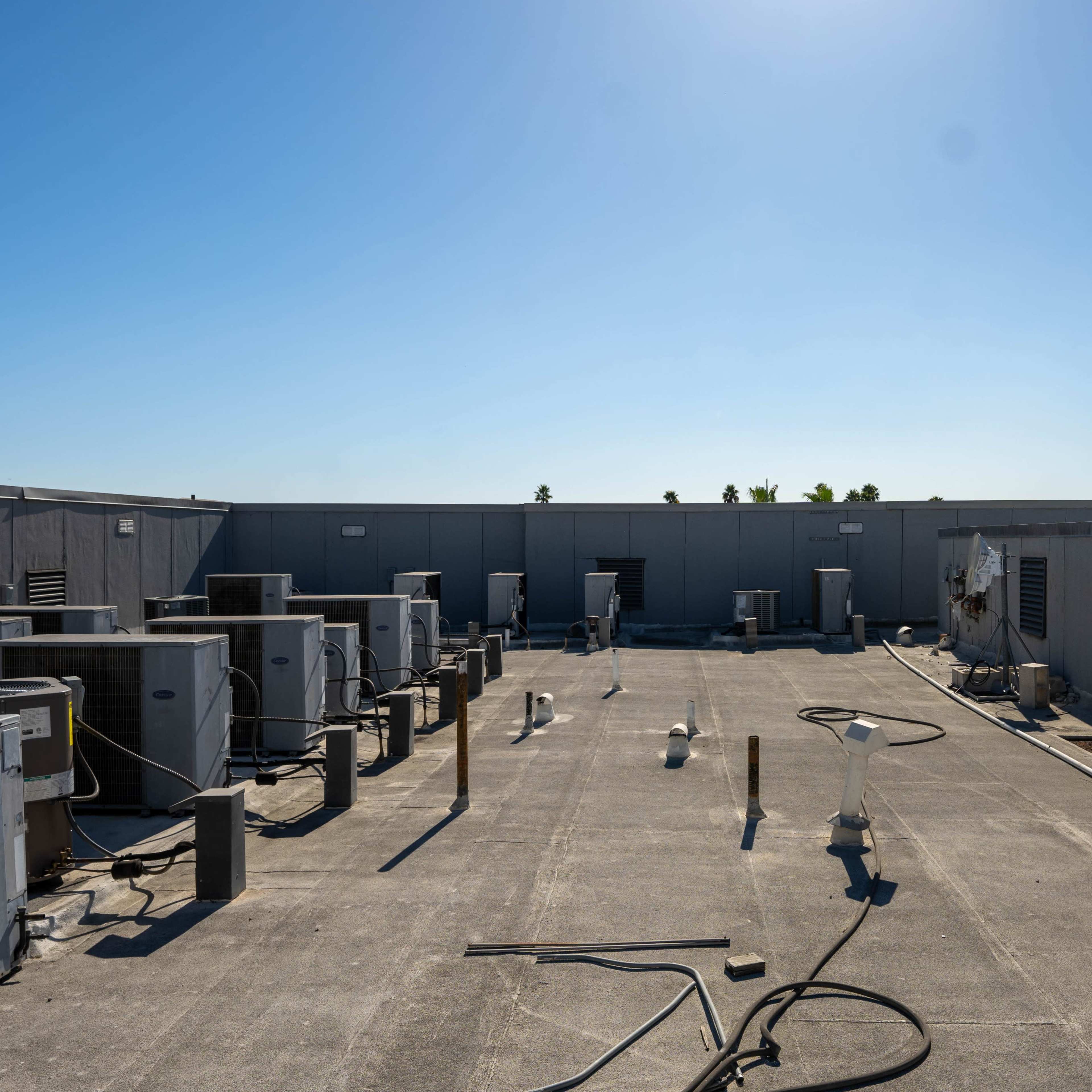 A flat rooftop equipped with multiple air conditioning units and various vent pipes under a clear blue sky.