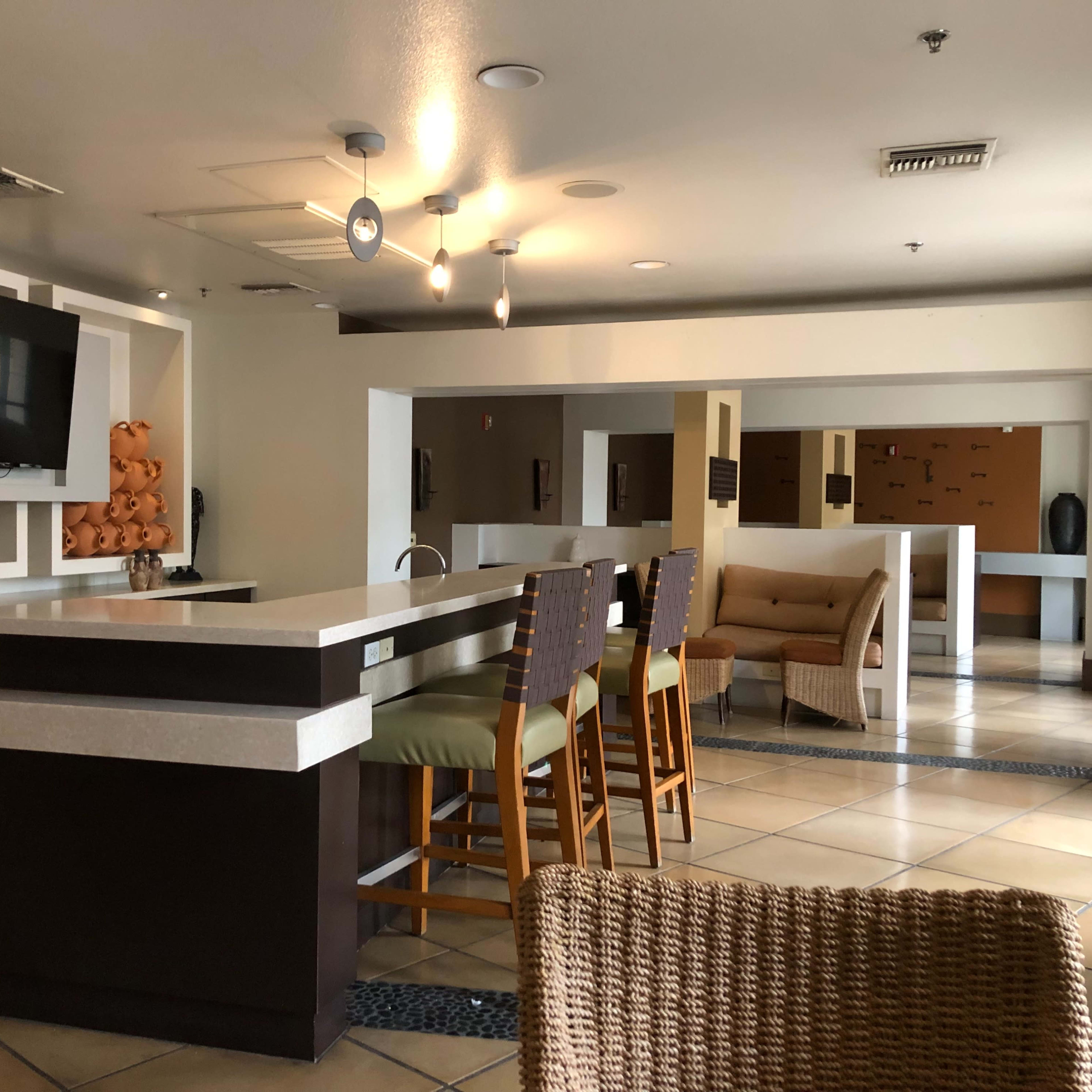 A modern lobby area with a bar counter, seating, and a large television mounted on the wall.