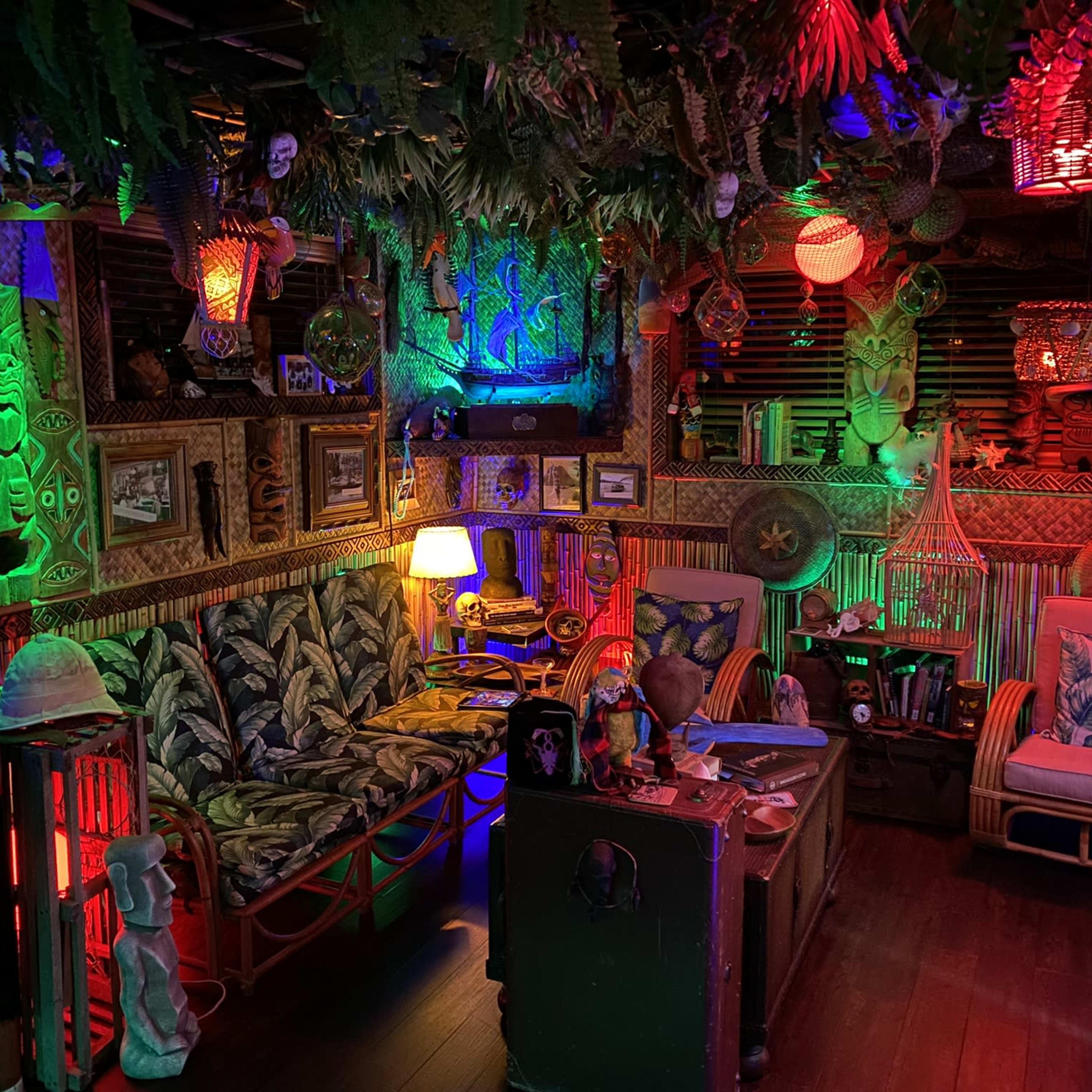 A cozy room decorated in a tropical theme with colorful lighting, tiki masks, and lush greenery.