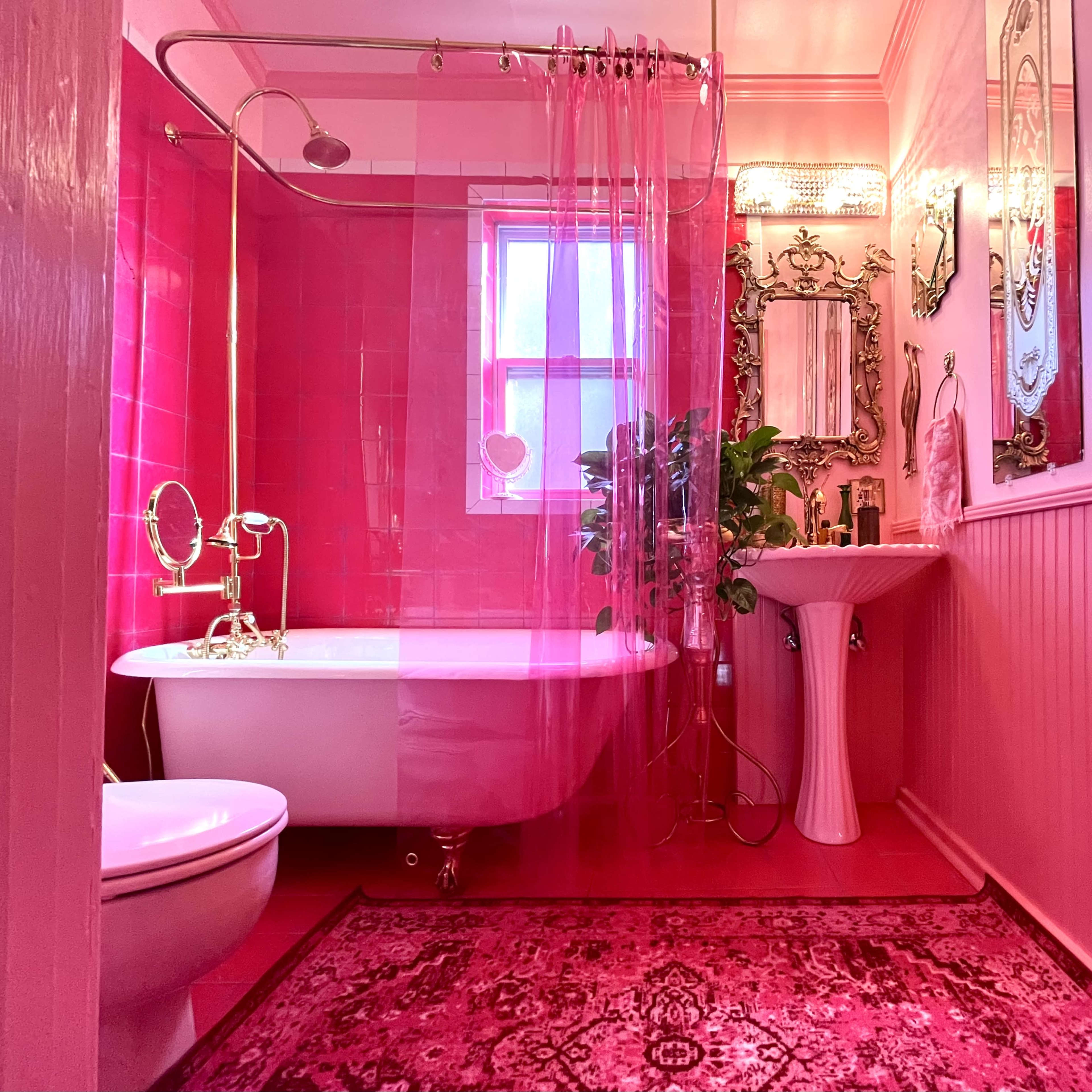 The bathroom features a pink color scheme with a clawfoot tub, a pedestal sink, and a plush rug.