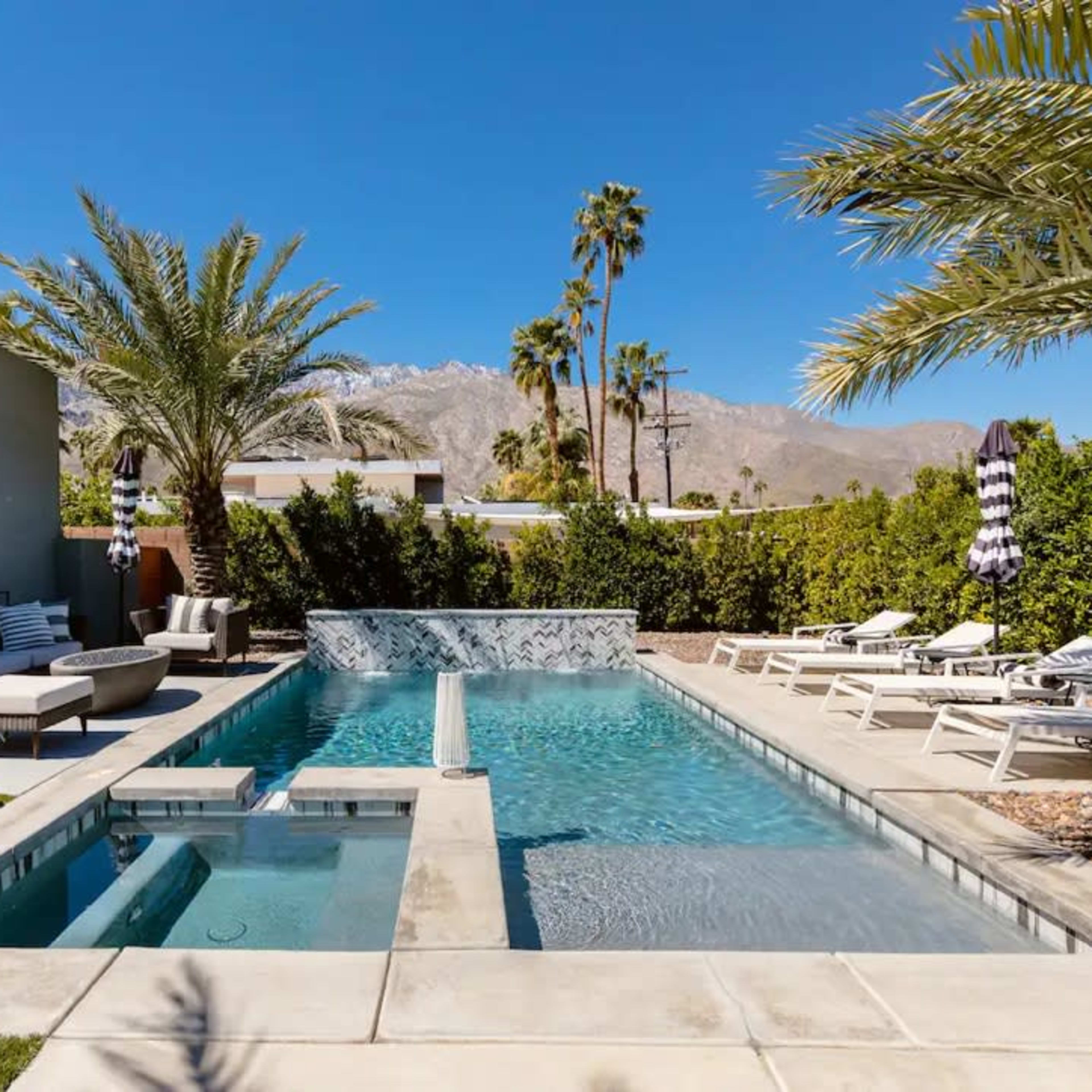 A modern backyard with a swimming pool, spa, palm trees, lounge chairs, and a large yellow rubber duck.