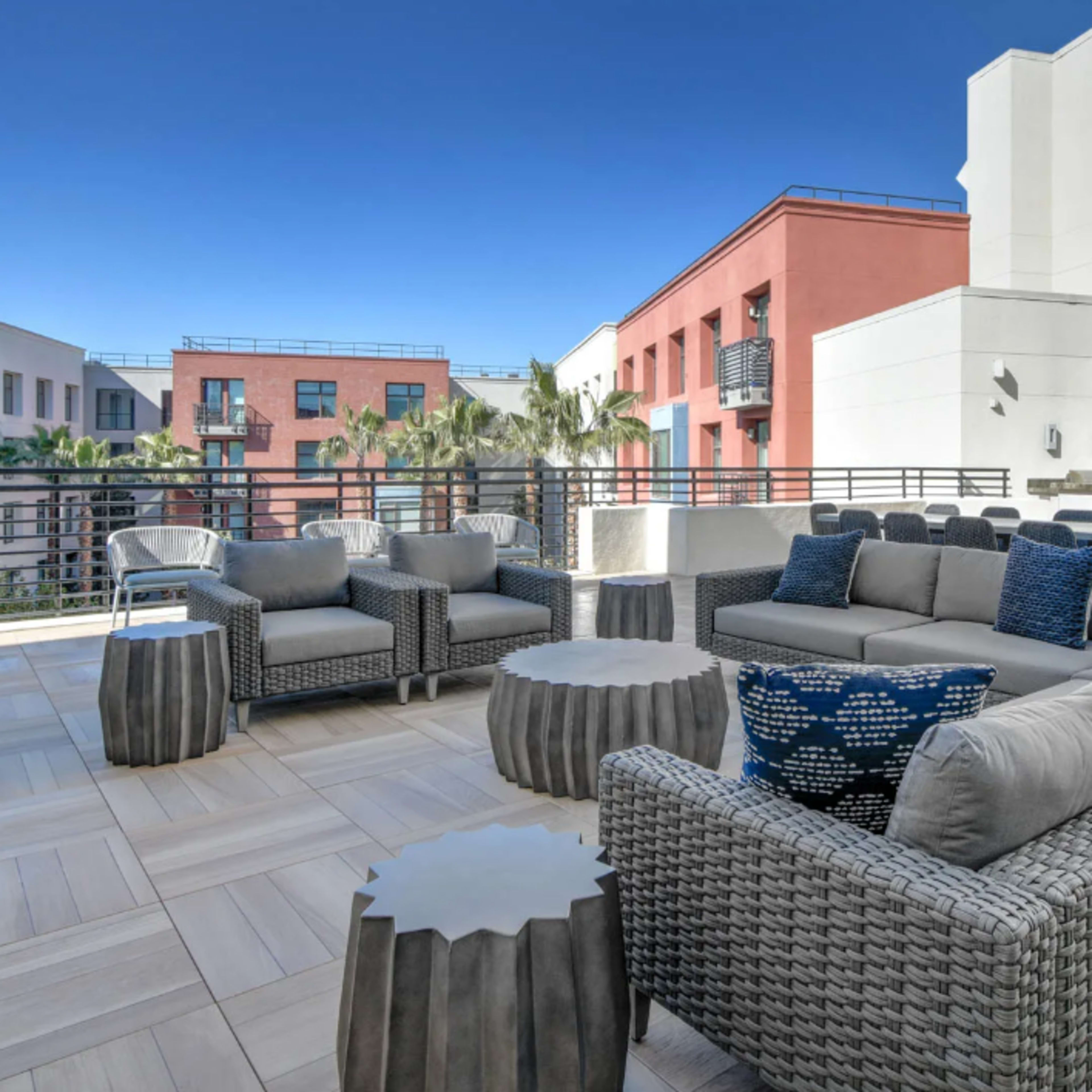 A modern outdoor lounge area featuring woven furniture, circular tables, and clear blue skies in the background.