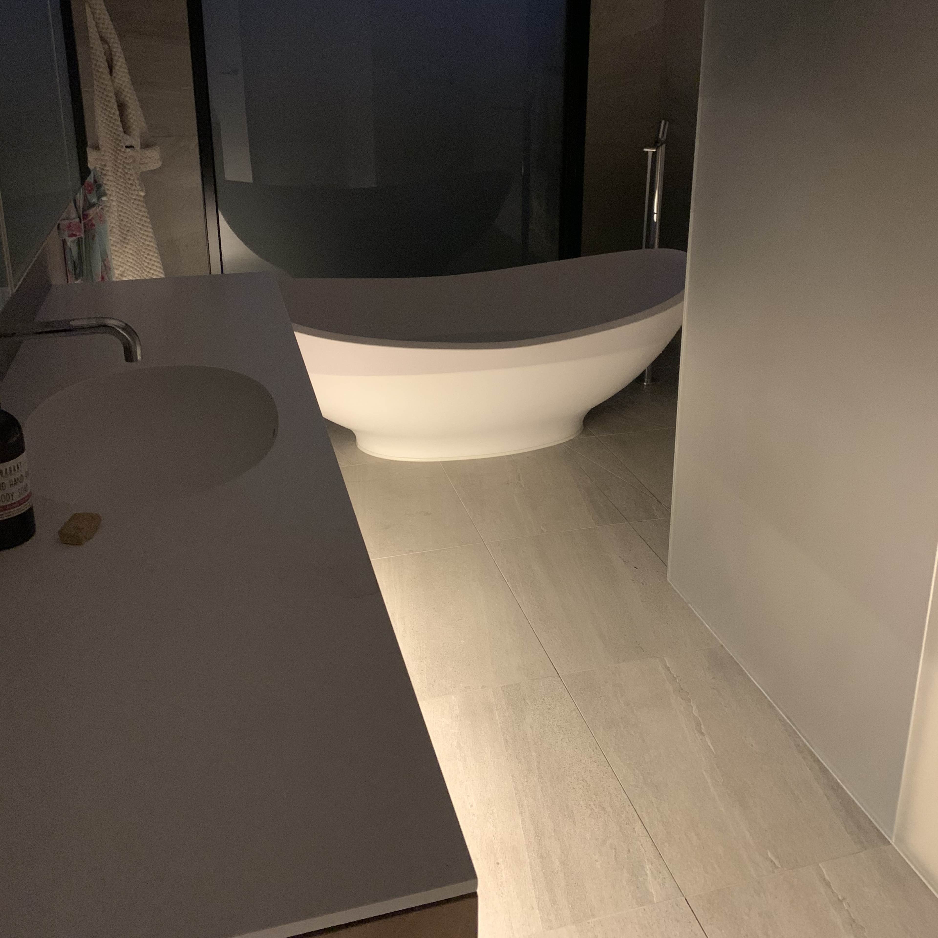 A modern bathroom with a freestanding bathtub, a large mirror, and a shower area, all illuminated by soft light.
