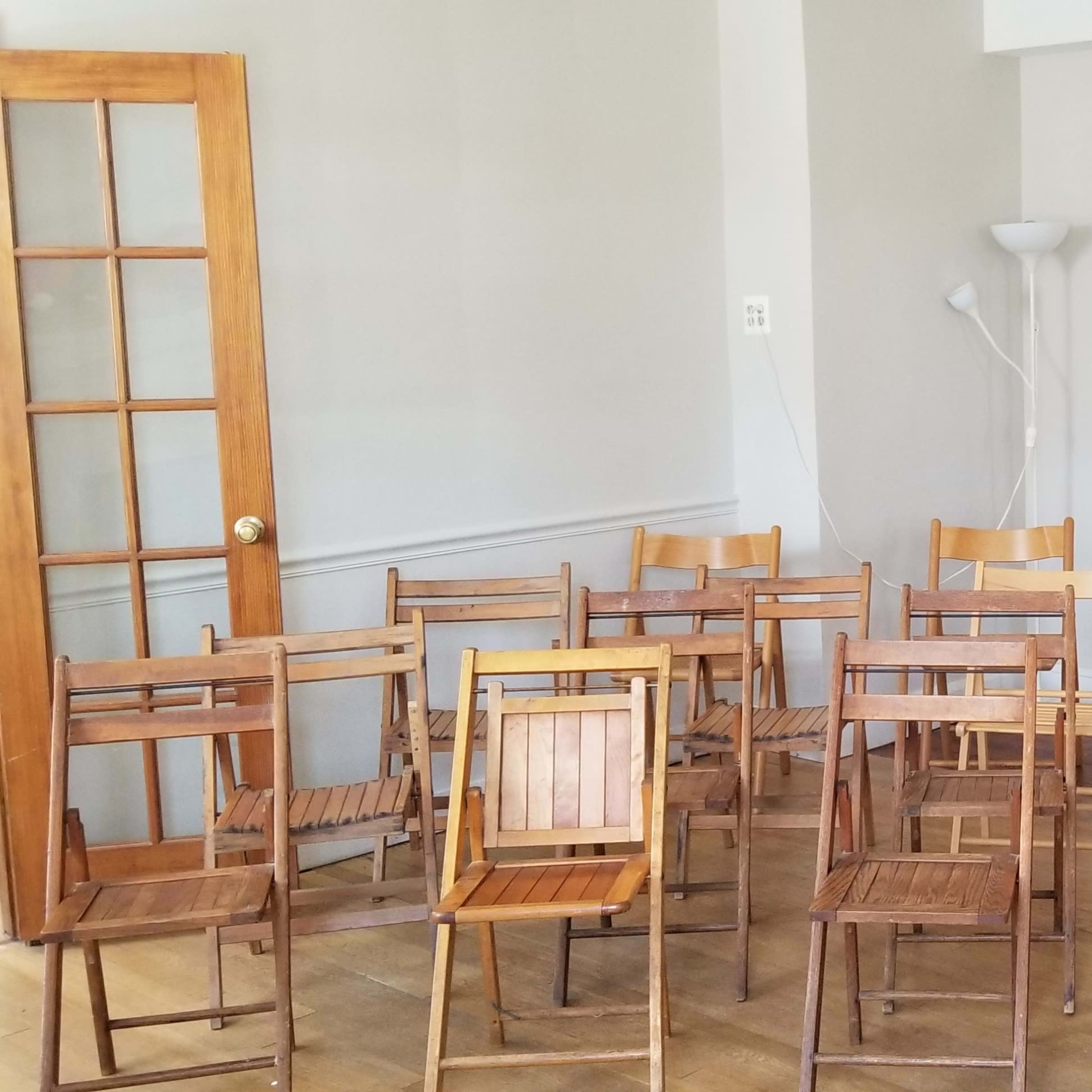 A group of wooden folding chairs is arranged in a room beside a folding screen and a lamp.