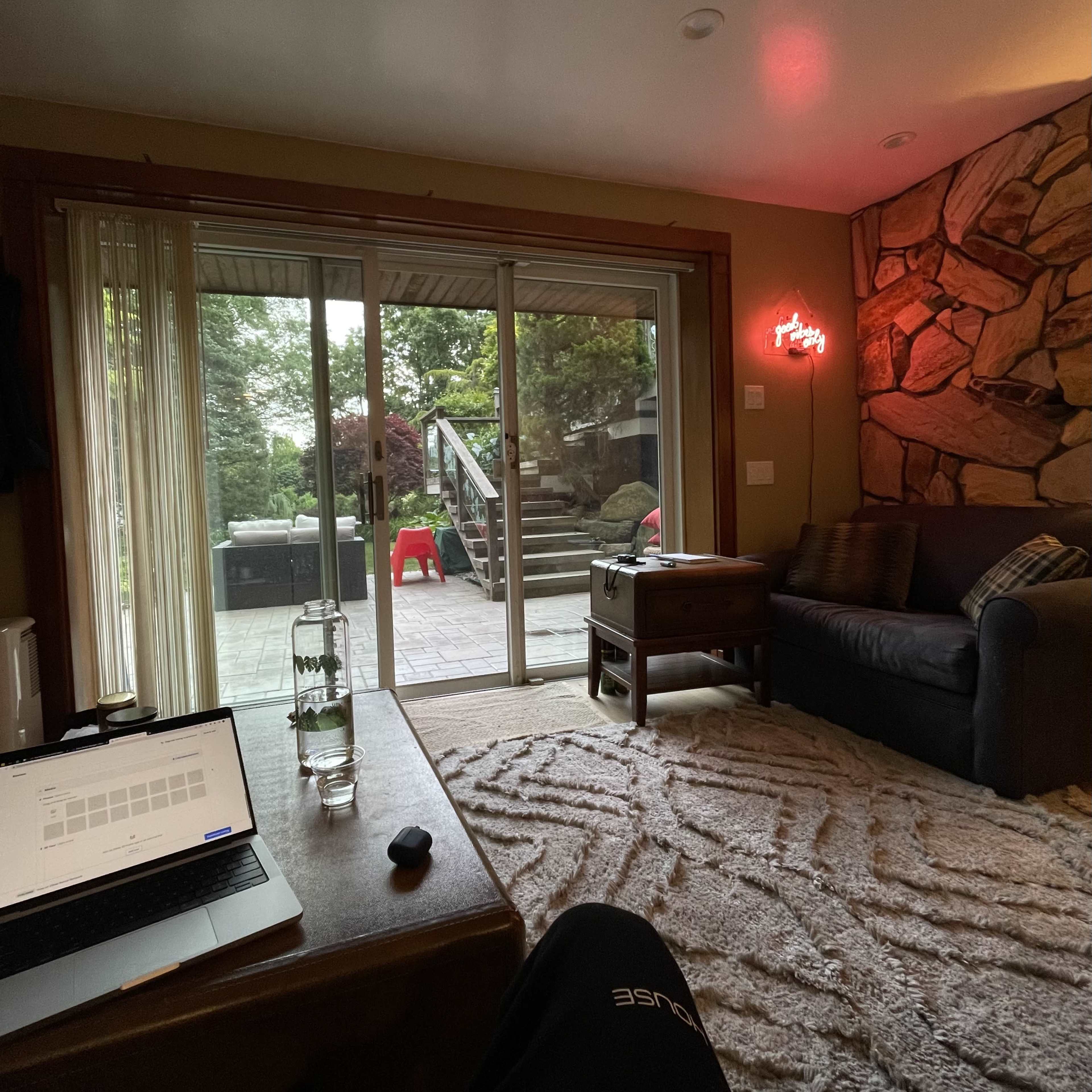 A living room features a sofa, a wooden table with a laptop, and glass doors leading to an outdoor patio.