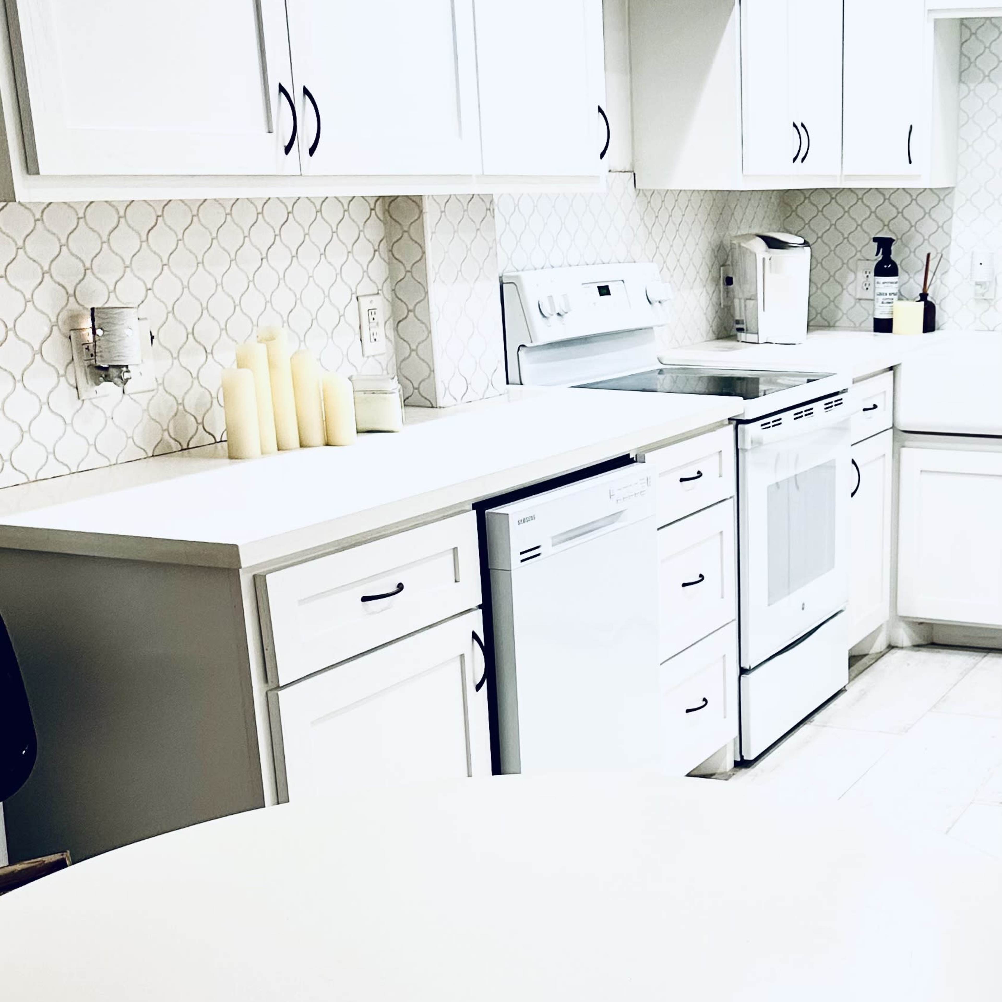A modern kitchen with white cabinetry, a gas stove, a dishwasher, and a round dining table in the foreground.