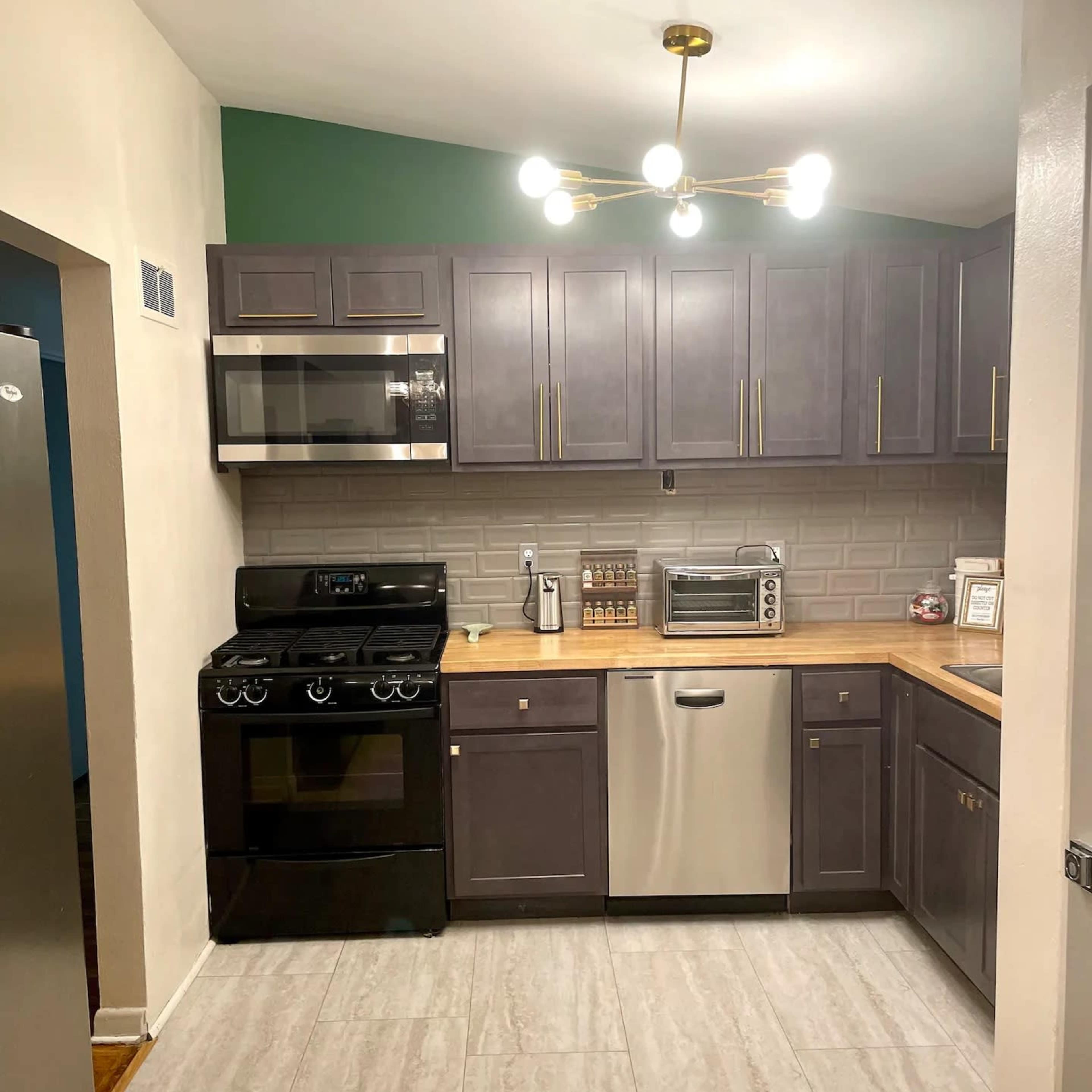 The kitchen features dark cabinetry, a stainless steel dishwasher, a black stove, and a countertop with a microwave and decorative jars.