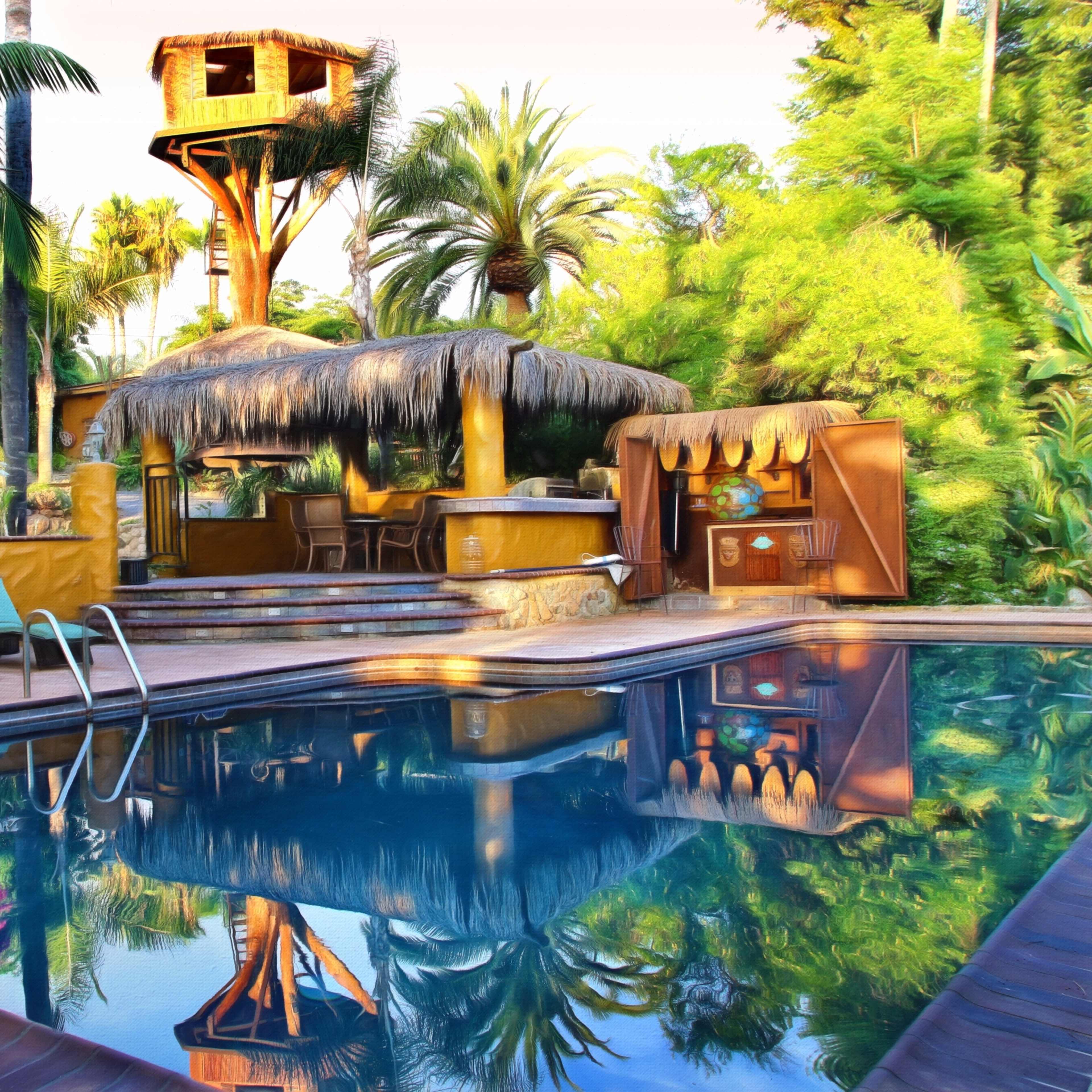 A swimming pool reflects a tropical landscape featuring a thatched roof bar and a raised treehouse surrounded by palm trees and vibrant plants.