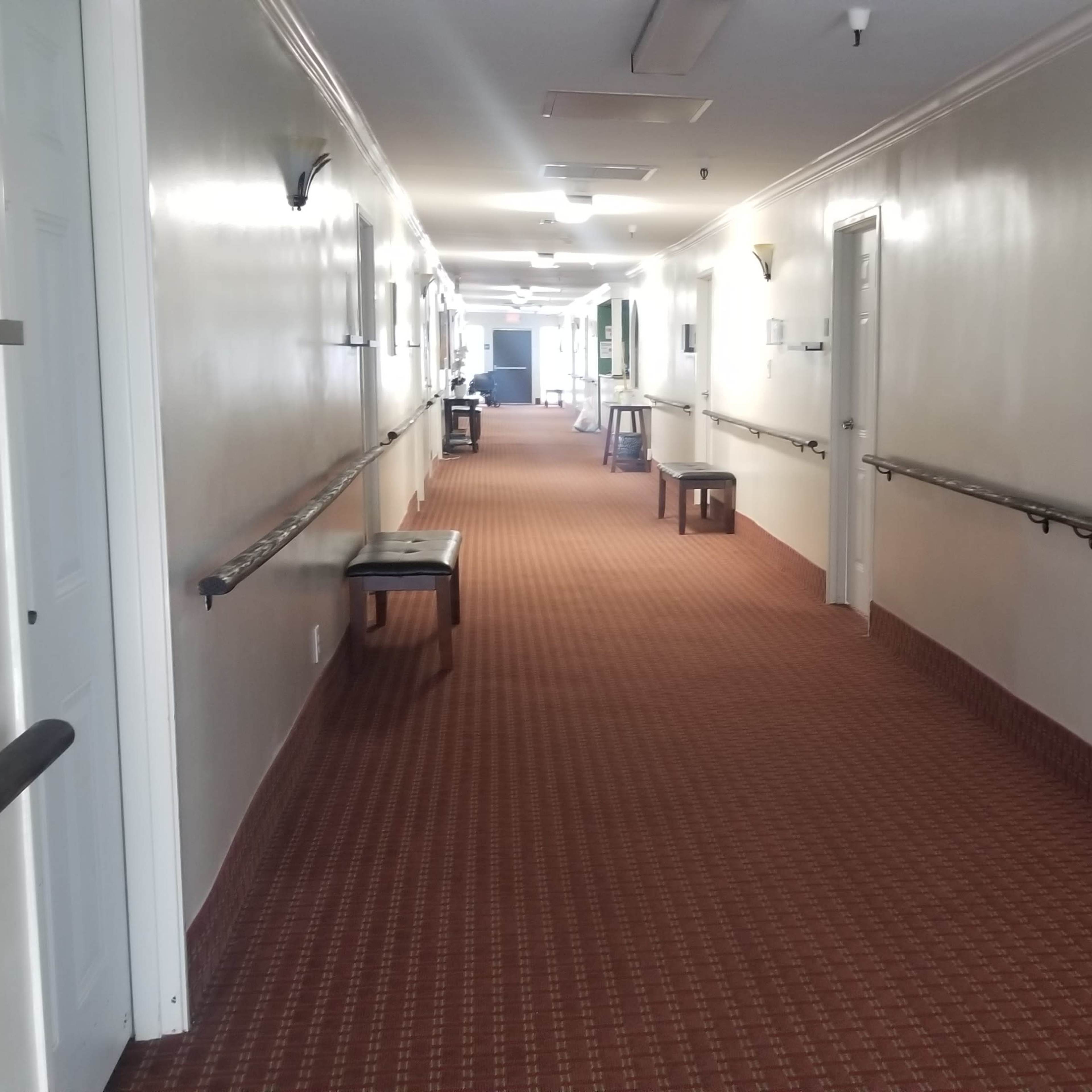 A long corridor with a patterned carpet, lined with white walls and several tables along the sides.
