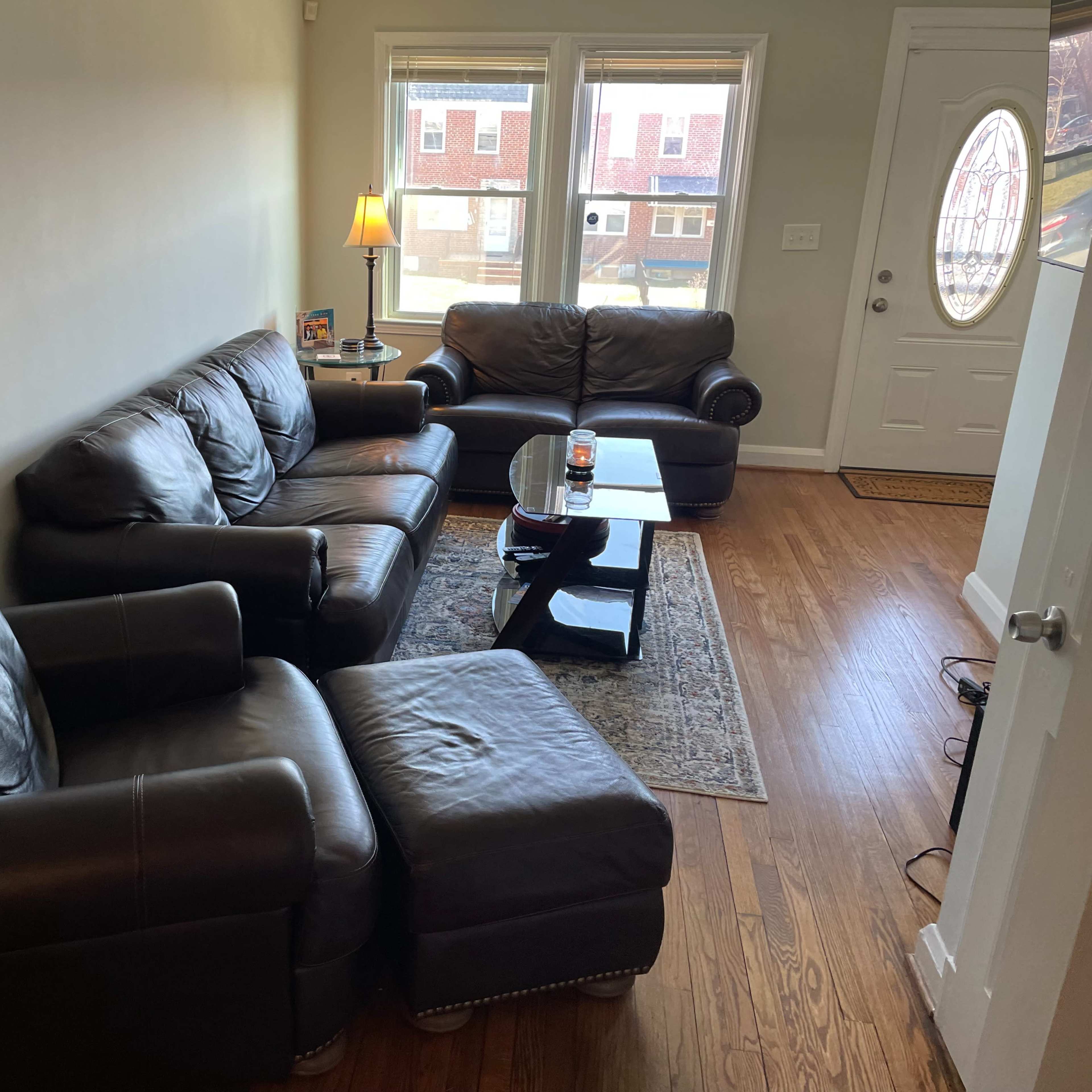 A cozy living room with a dark leather seating arrangement, a coffee table, and a door leading outside.