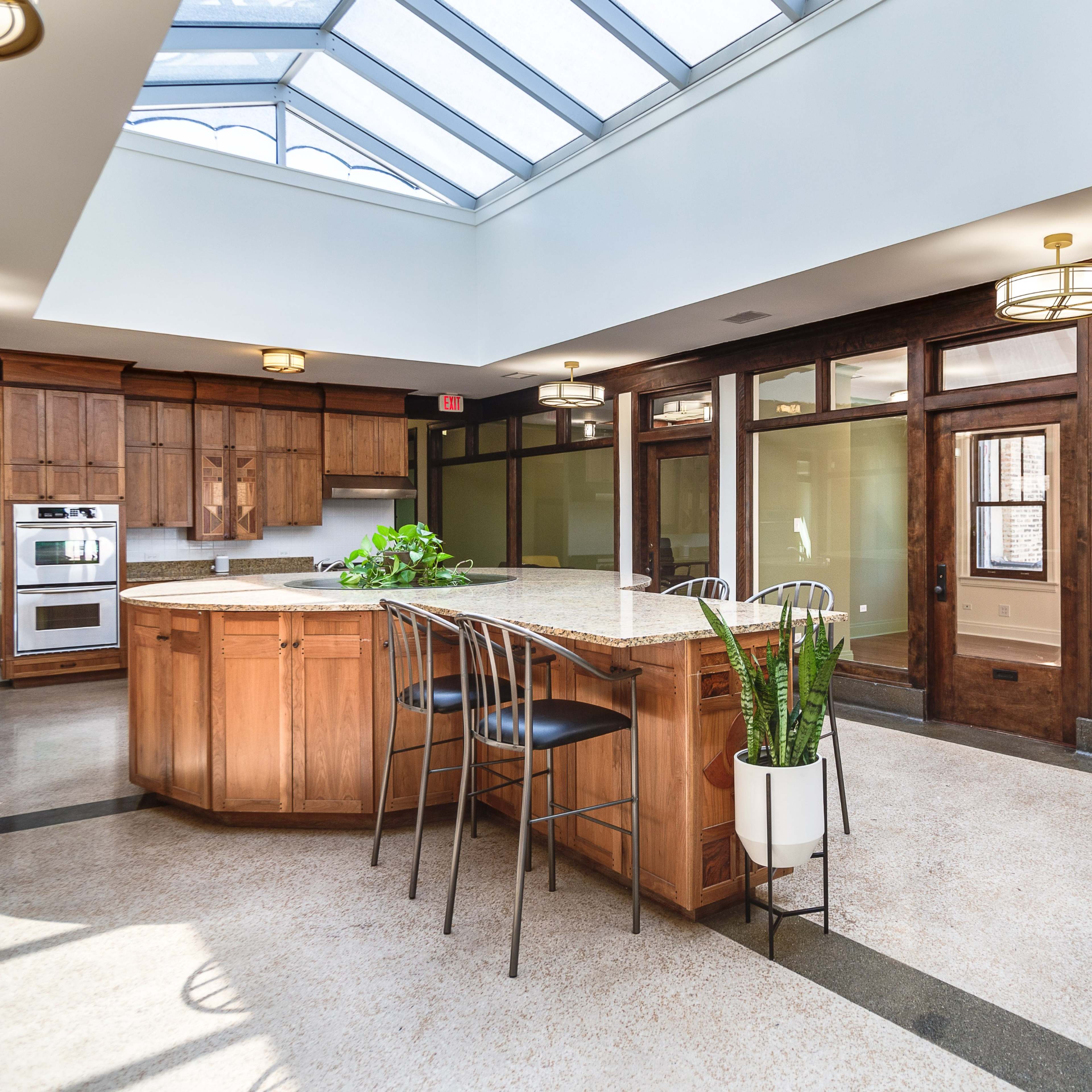 A spacious kitchen with a central island, wooden cabinetry, and large windows allowing natural light to enter.