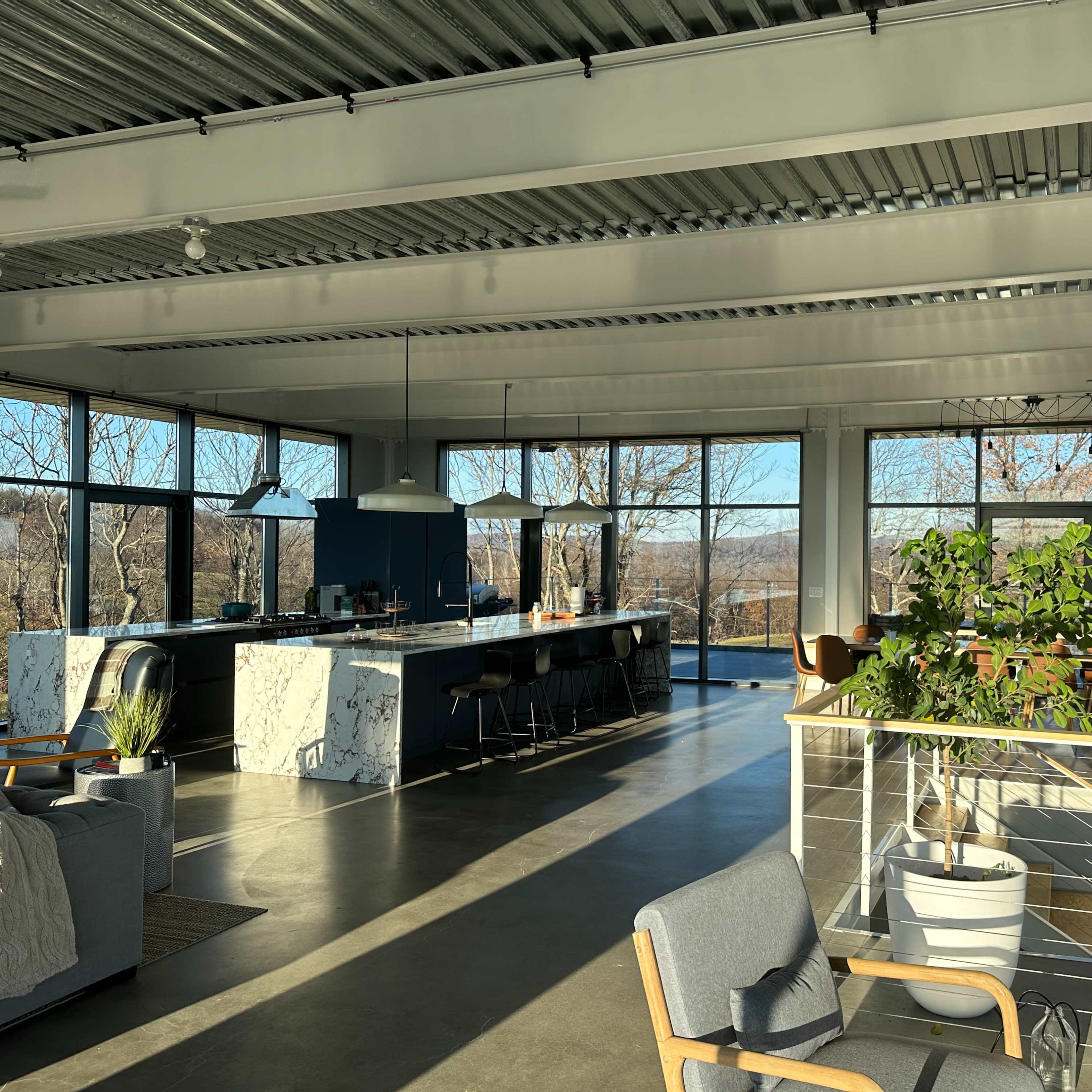 A spacious modern interior featuring a kitchen and dining area with large windows overlooking a natural landscape.