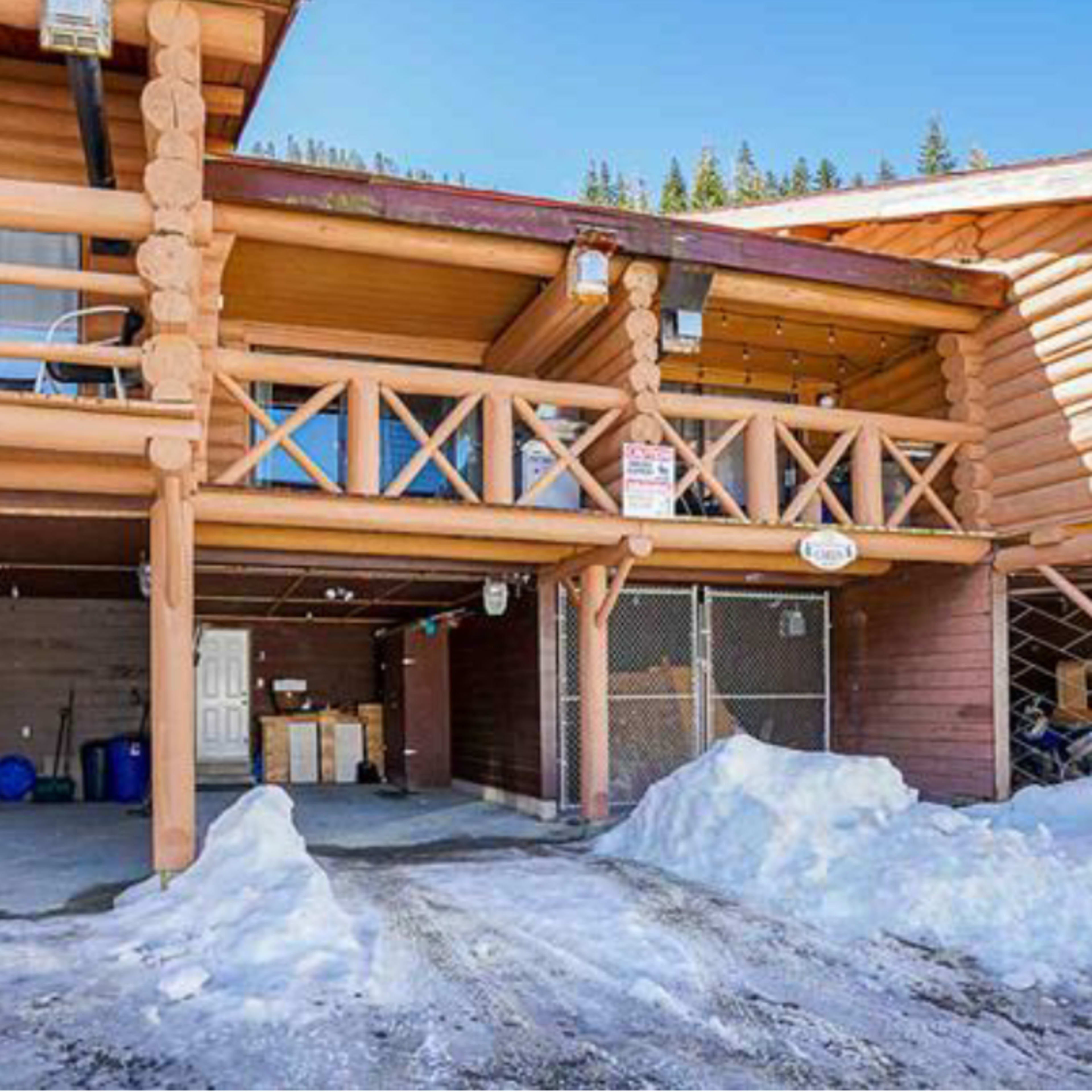 A log cabin-style building with a snow-covered driveway and covered parking area.