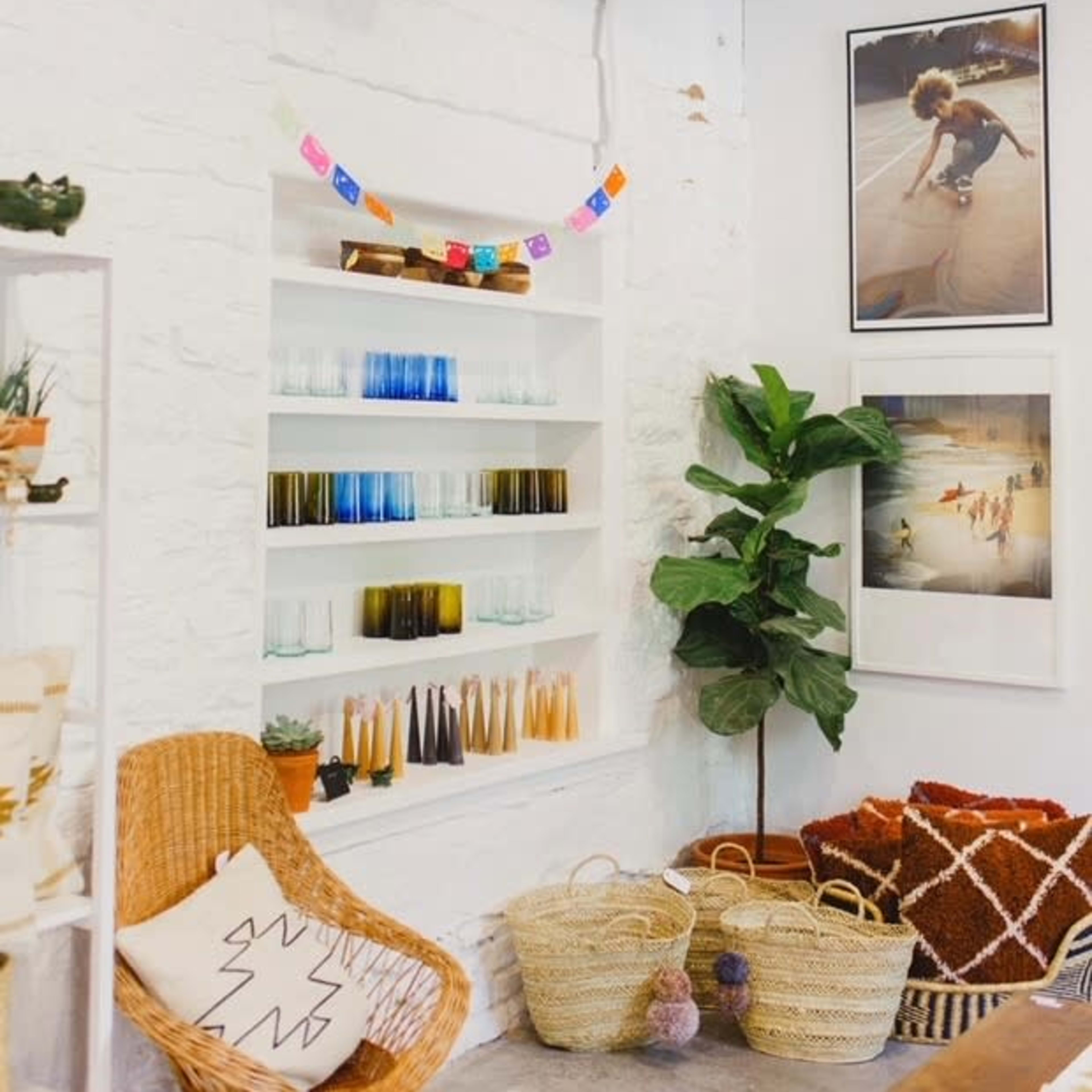 A cozy corner of a store featuring shelves of colorful glassware, decorative photos on the wall, plants, and woven baskets.