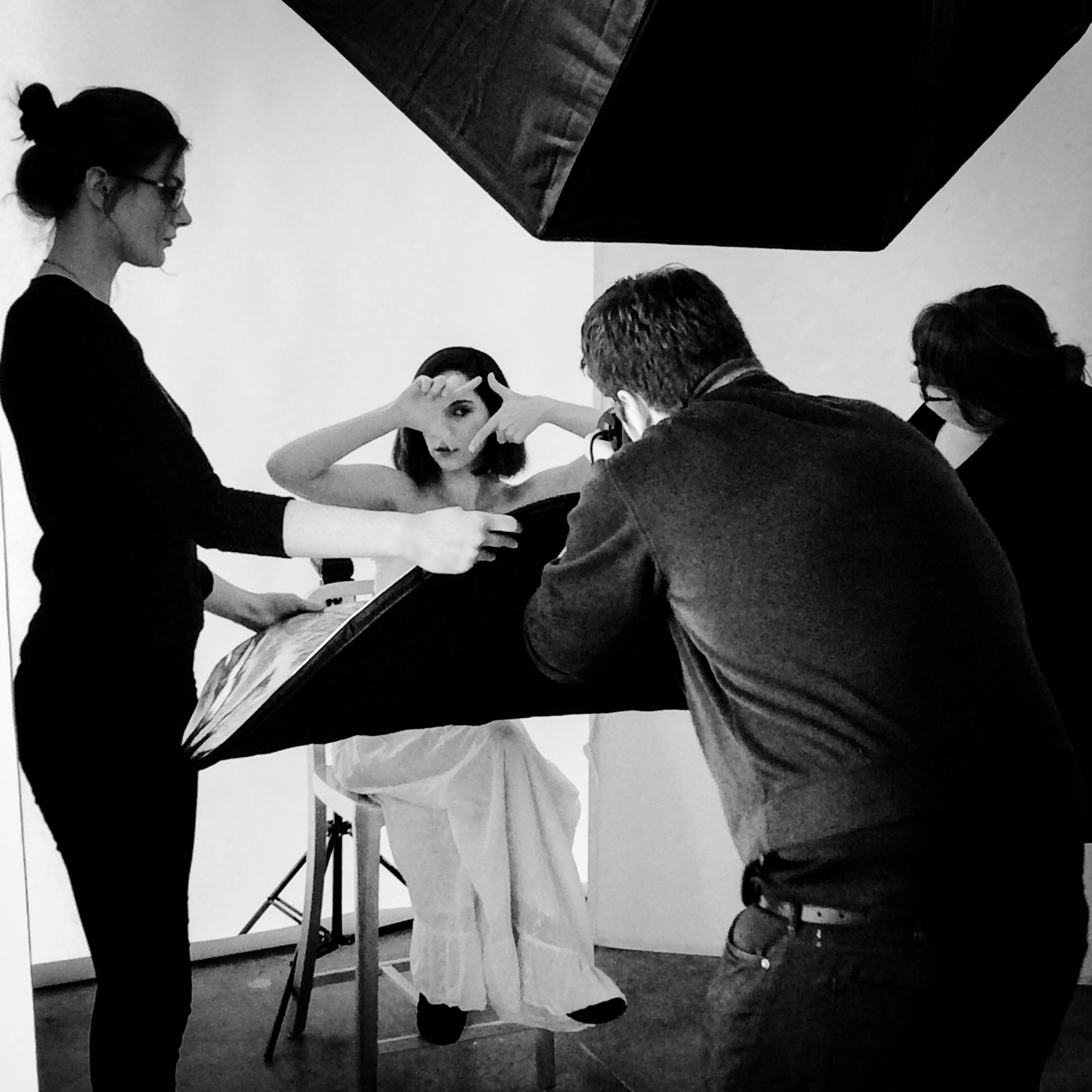 A model poses under studio lights while a team of photographers and assistants adjusts equipment around her.