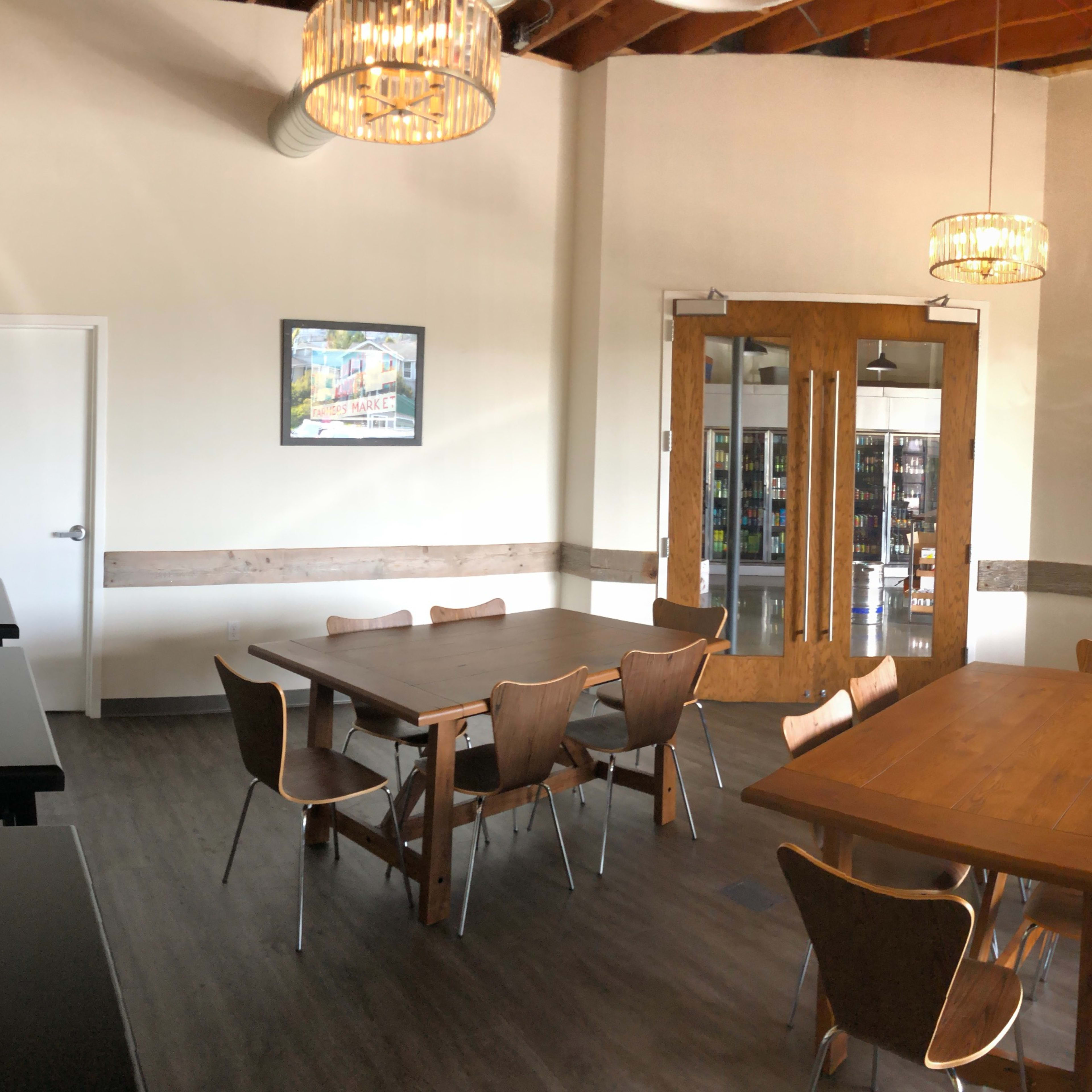 A modern meeting room with wooden tables, chairs, and a blue sofa, illuminated by chandelier lighting.