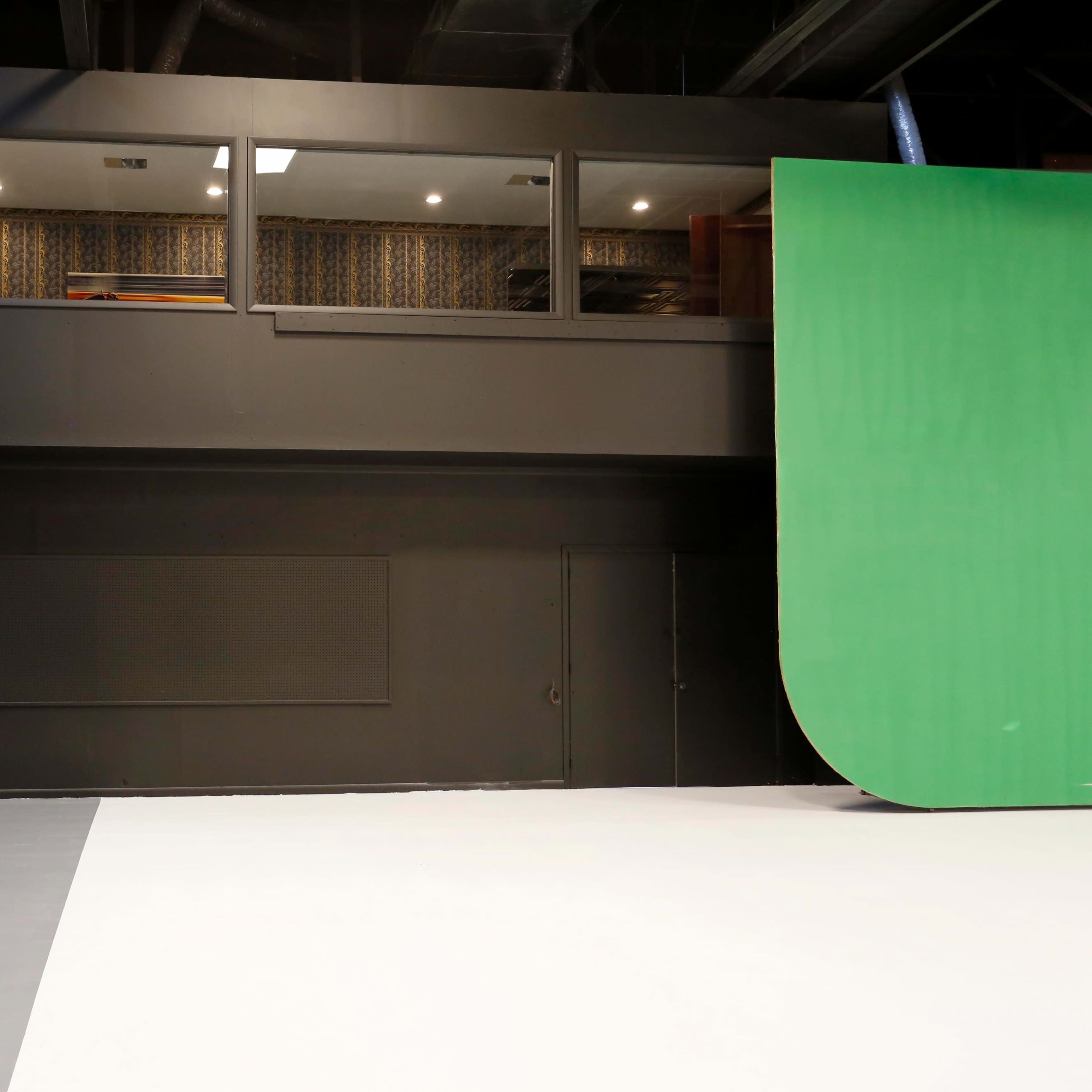 A film studio interior featuring a green screen on the right and a staircase leading to a viewing area above.