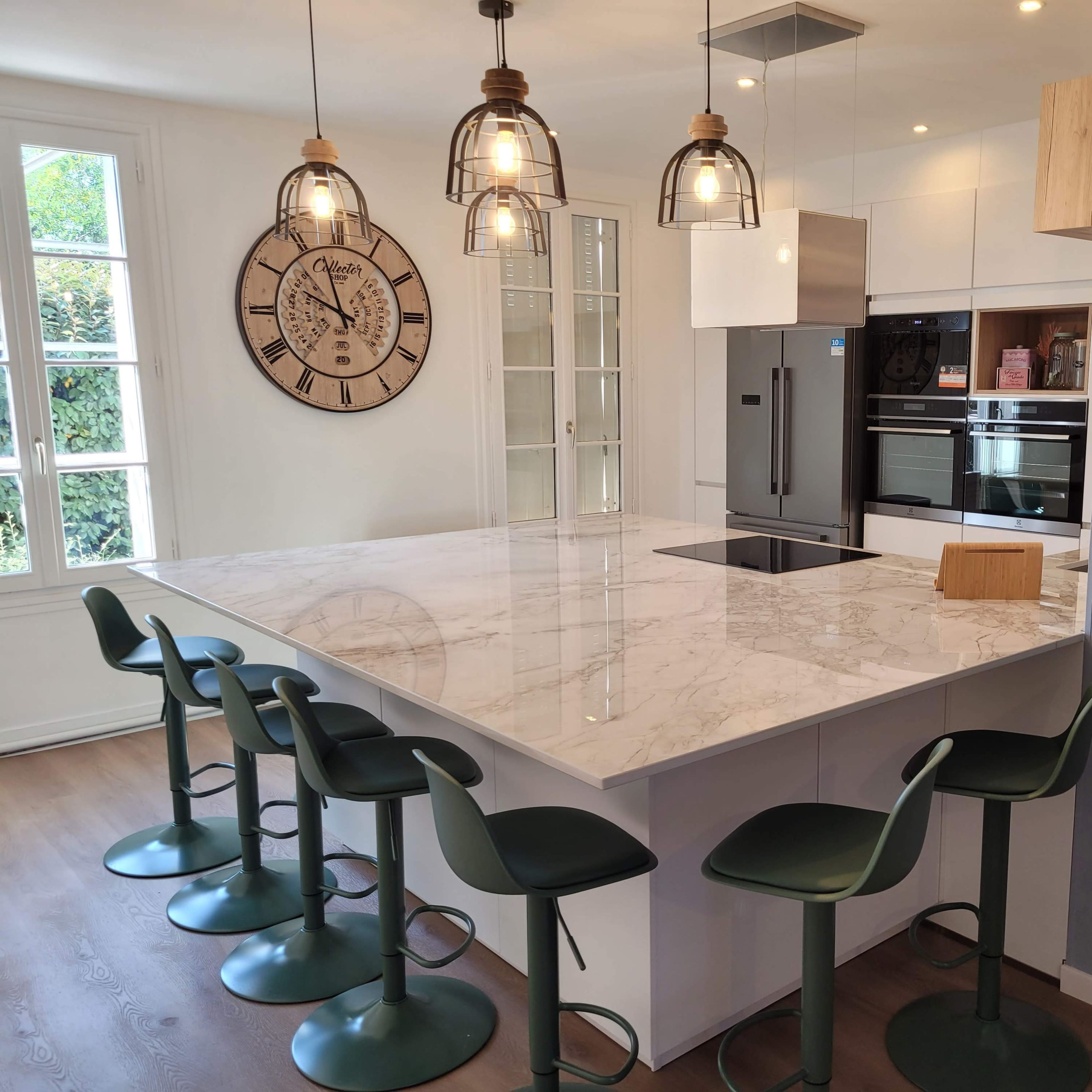 A modern kitchen with a marble island, green bar stools, and a large wall clock.