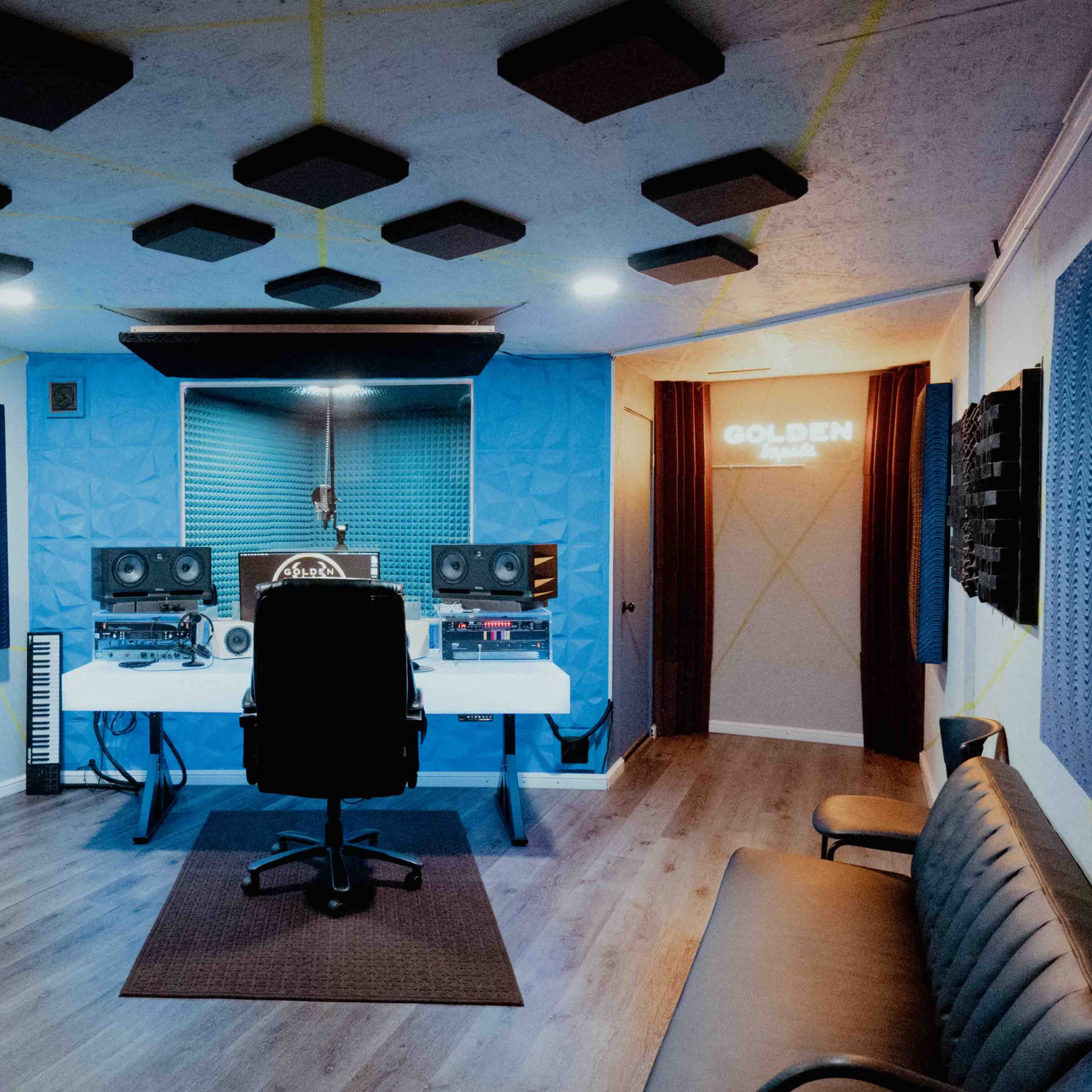 A soundproof recording studio features a central desk with audio equipment, a chair, and acoustic panels on the walls and ceiling.