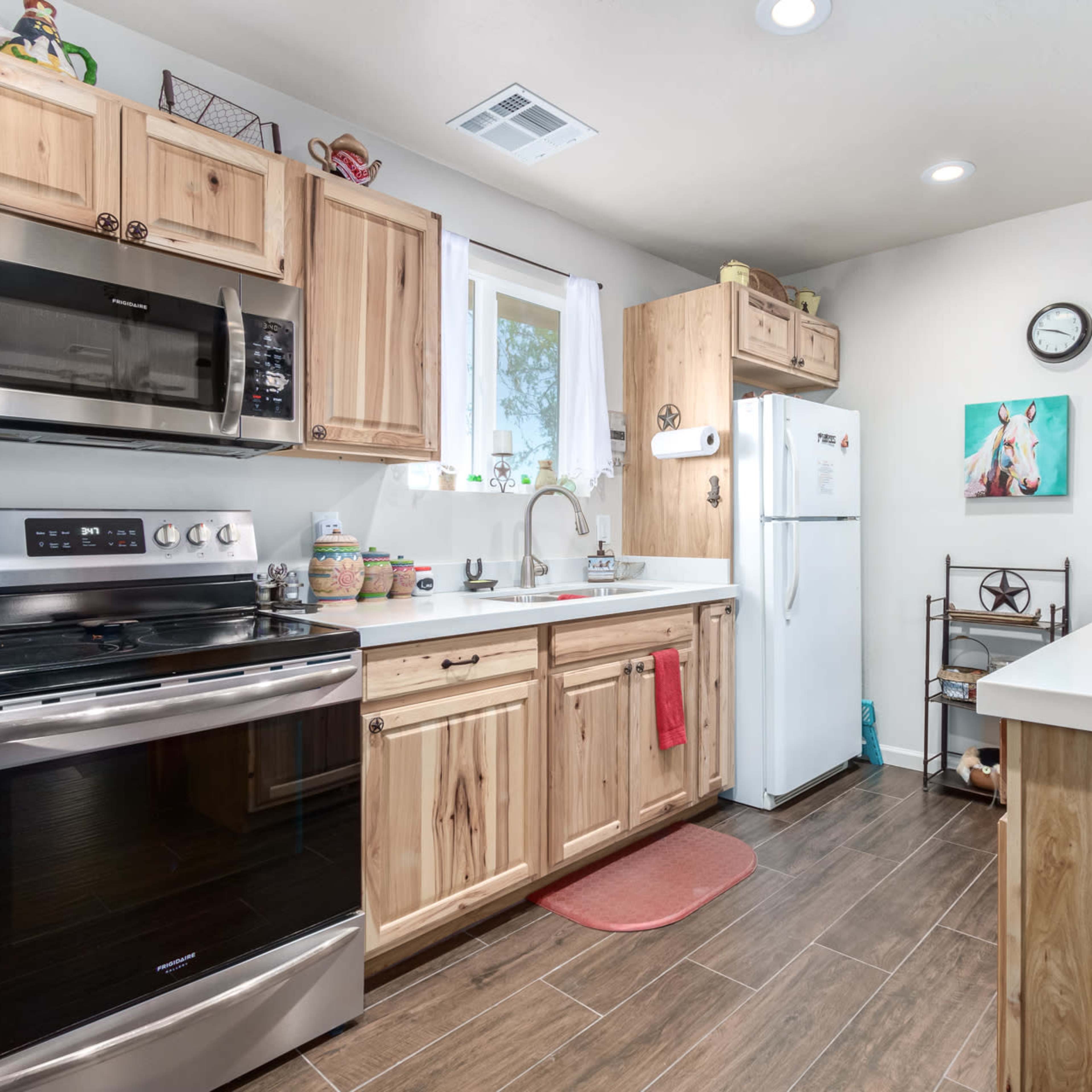 A modern kitchen features wooden cabinetry, stainless steel appliances, and a white countertop with a window allowing natural light.