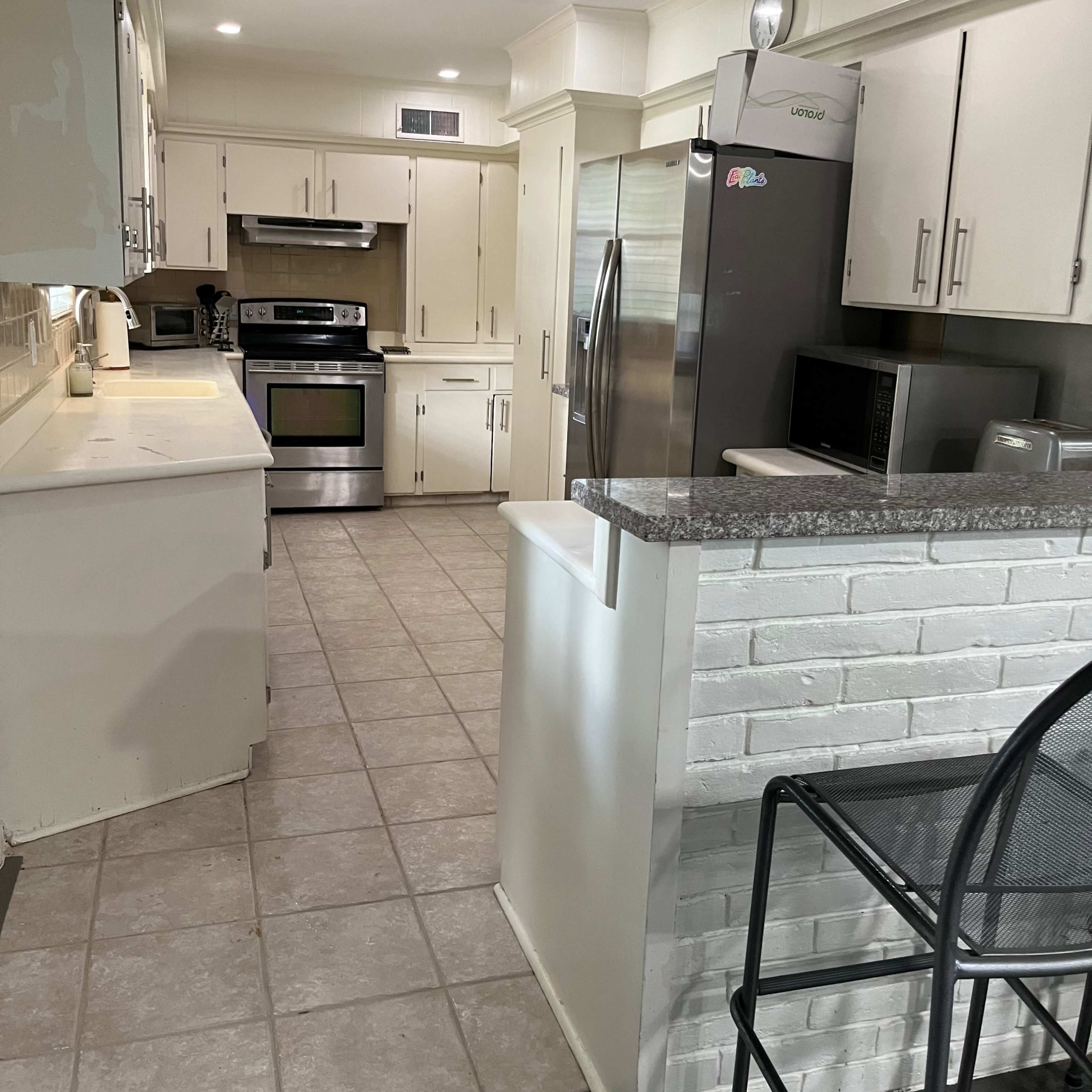 A modern kitchen with stainless steel appliances, beige cabinets, and tiled flooring.