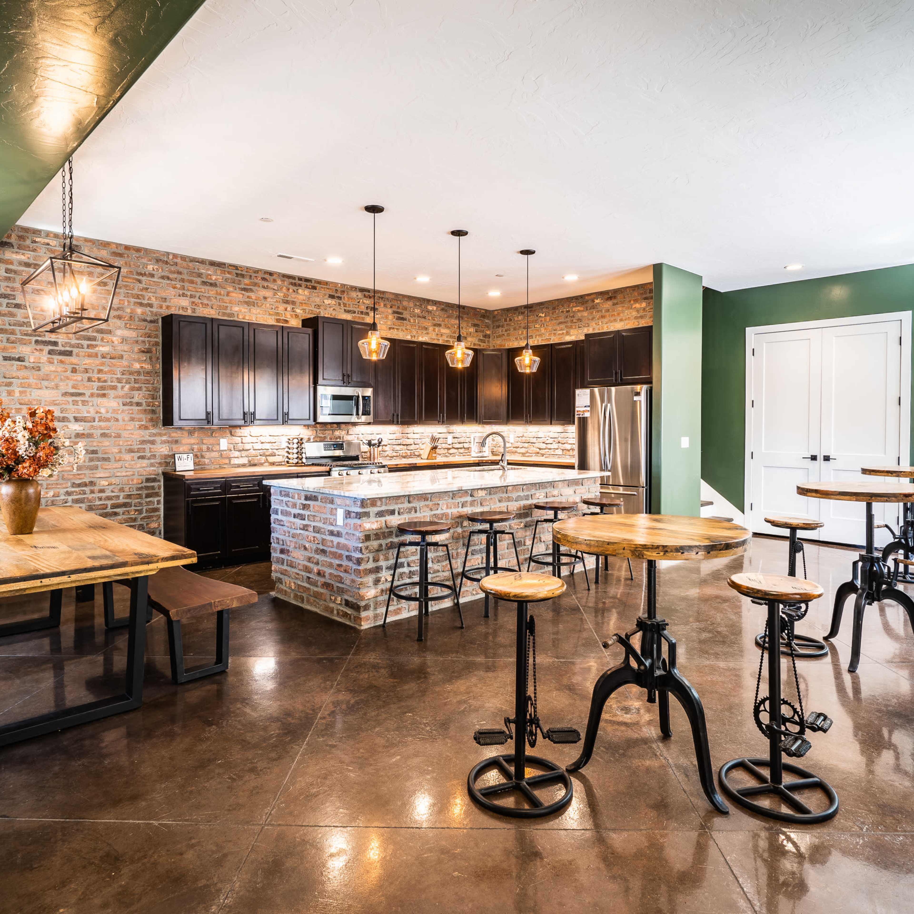 A modern kitchen and dining area featuring a brick accent wall, dark cabinetry, a large island, and several high-top tables.