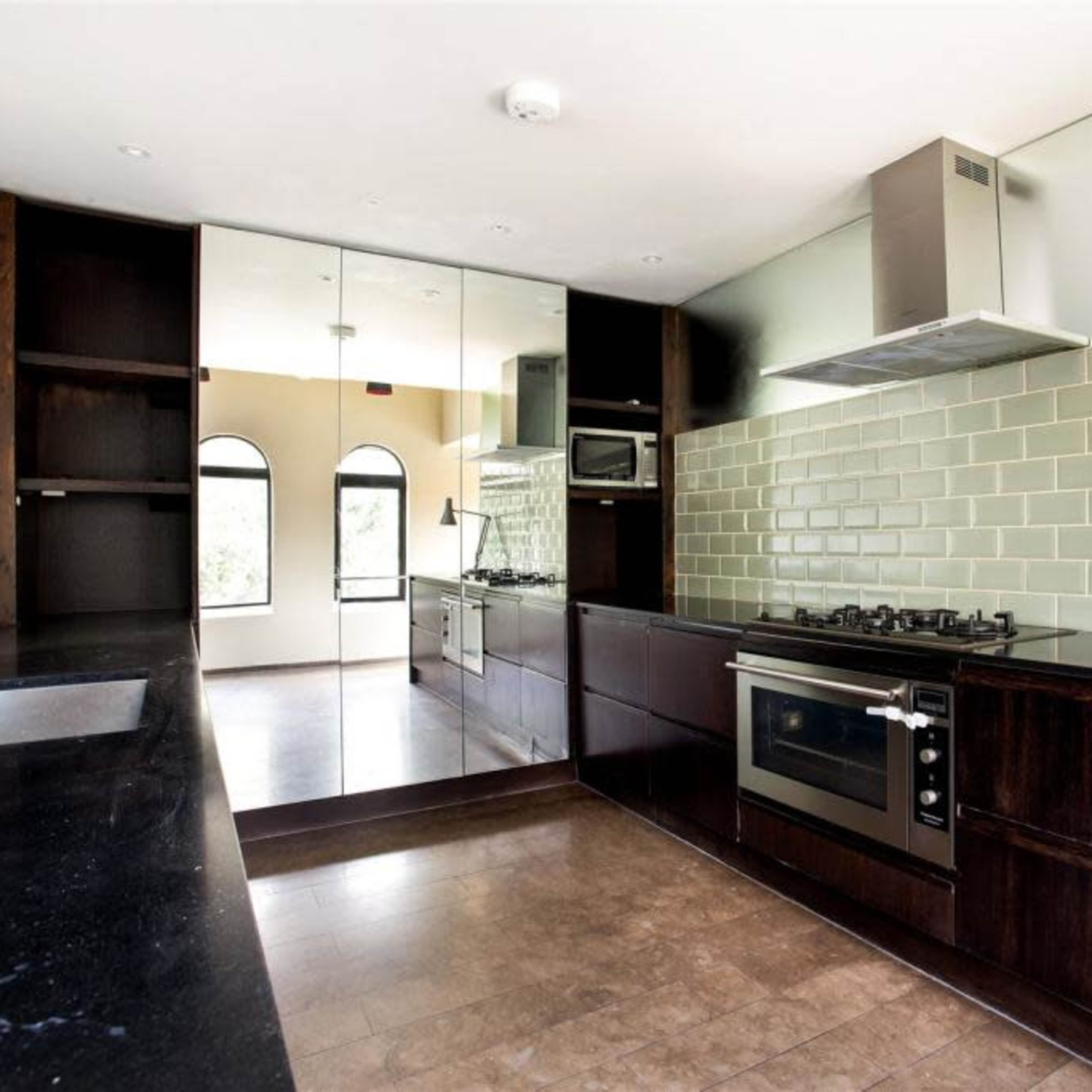 A modern kitchen with dark cabinetry, a mirrored wall, and a green tile backsplash.