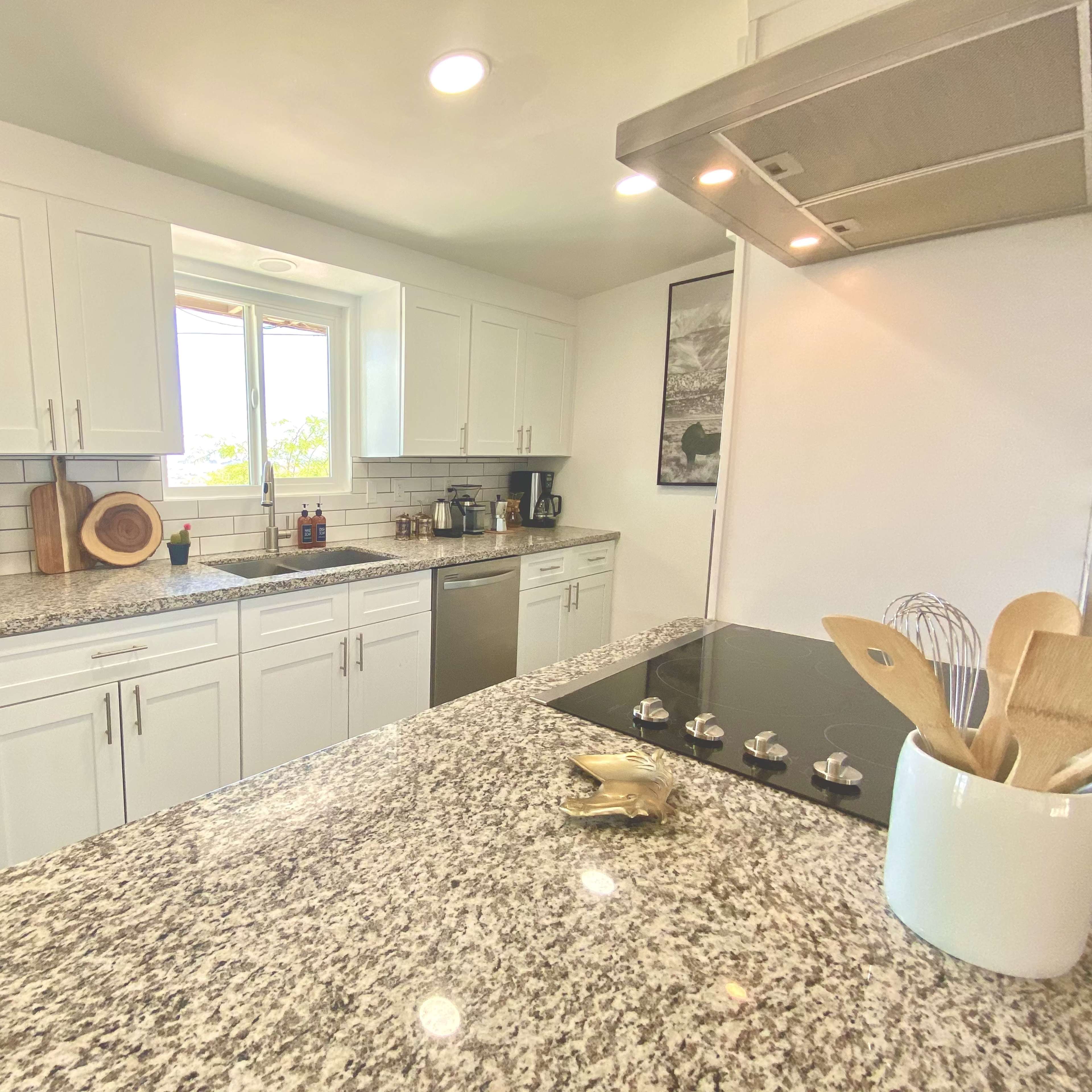 A modern kitchen featuring white cabinets, a granite countertop, stainless steel appliances, and a window above the sink.