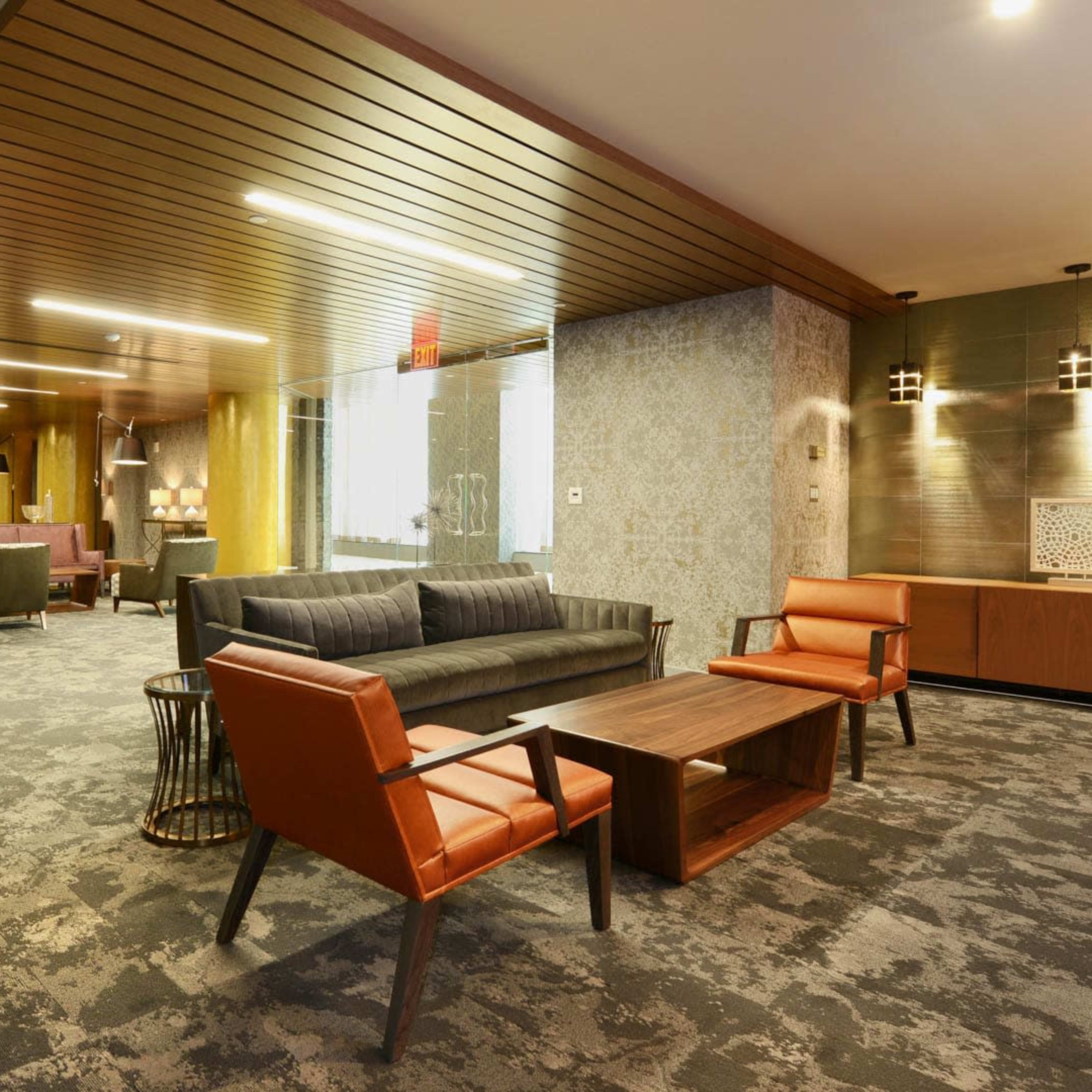 A modern lounge area featuring a gray sofa, orange chairs, a wooden coffee table, and ambient lighting.