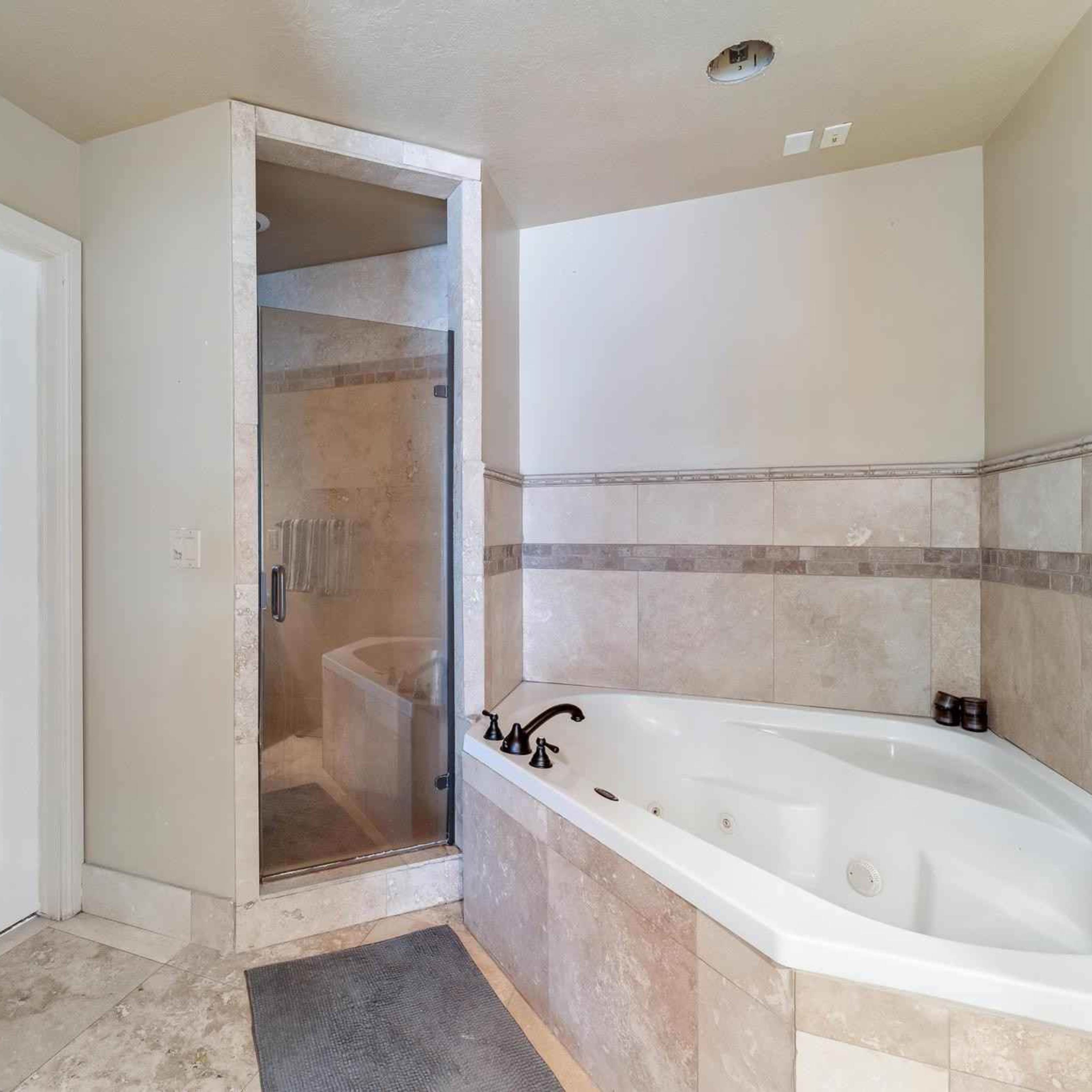 A bathroom with a glass shower enclosure, a large white bathtub, and tiled walls.