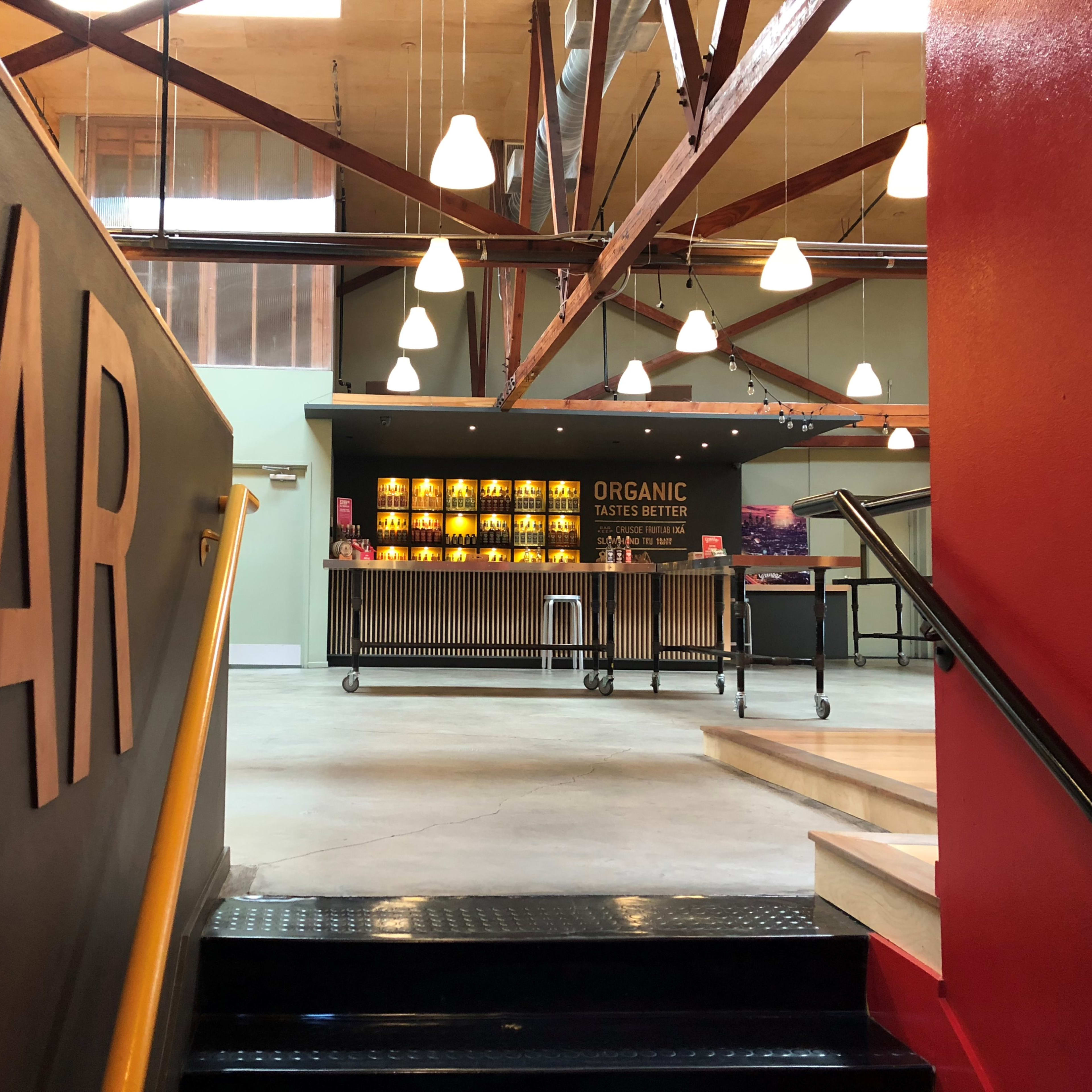 A staircase leads up to a well-lit bar area featuring a wooden counter with shelves displaying organic products.