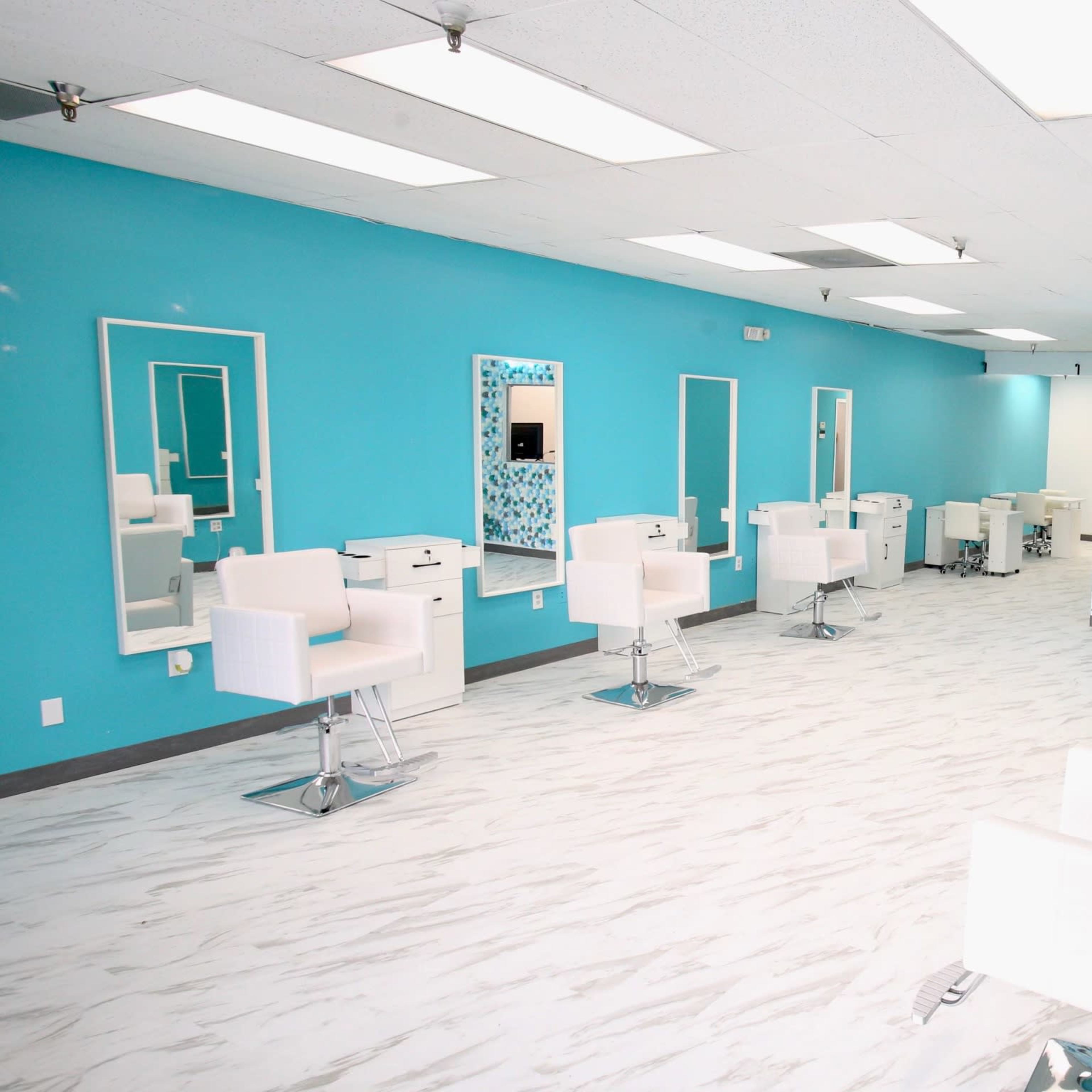 A brightly lit hair salon with turquoise walls, white styling stations, and modern chairs arranged neatly throughout the space.