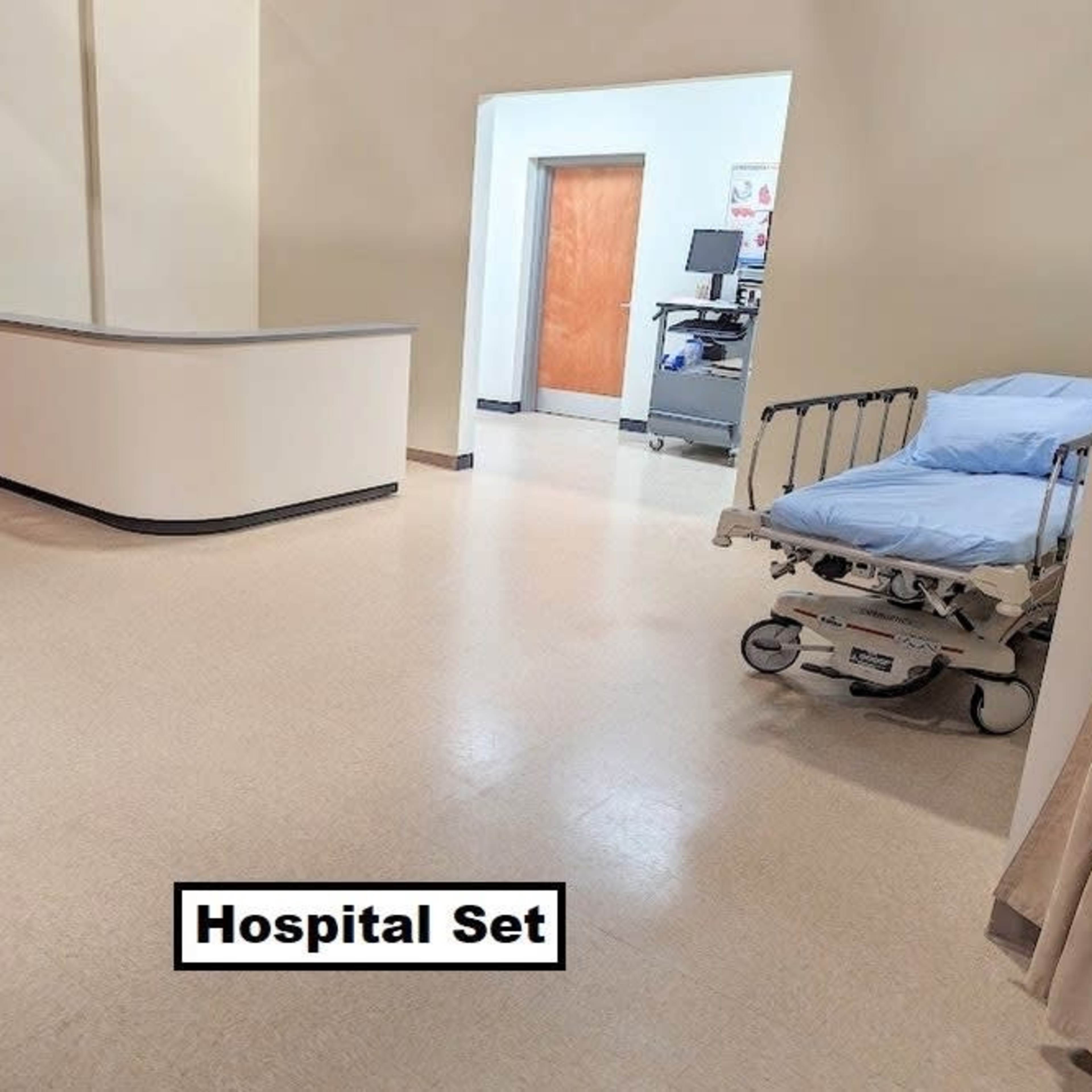 A hospital set with a reception area, an empty patient bed, and a doorway leading to another room.