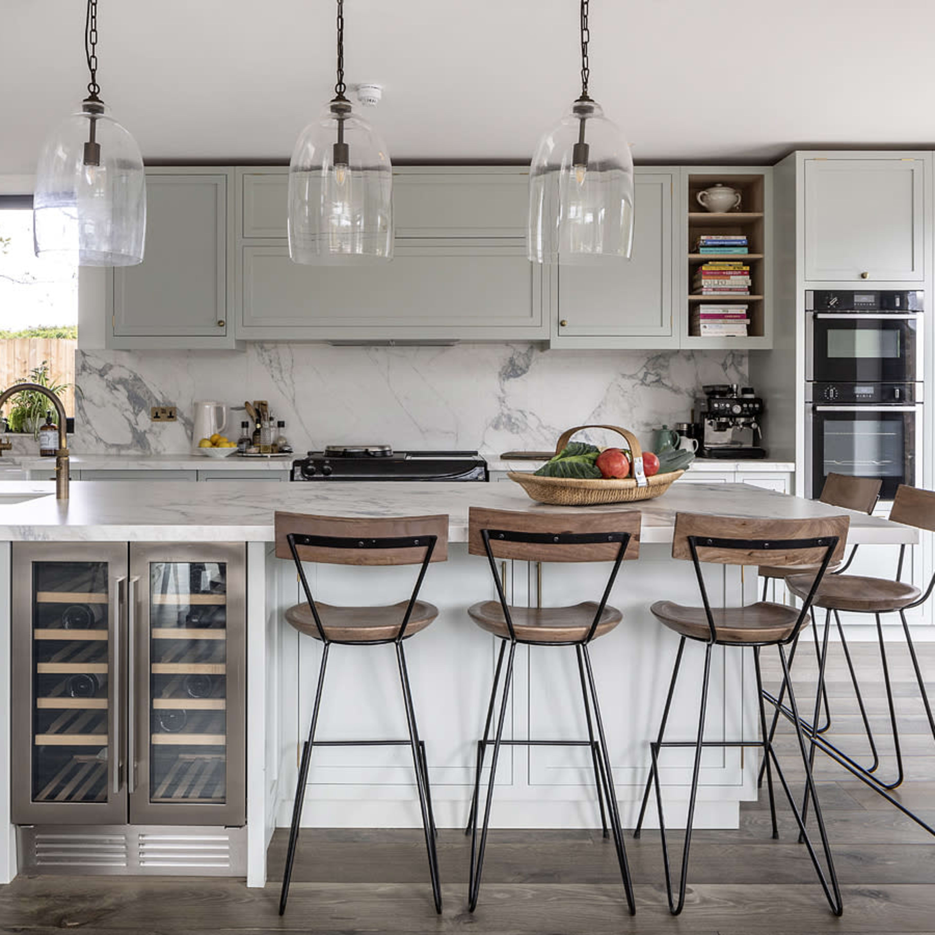 A modern kitchen features a large island with a marble countertop, bar stools, and pendant lighting, alongside cabinets and a stainless steel refrigerator.