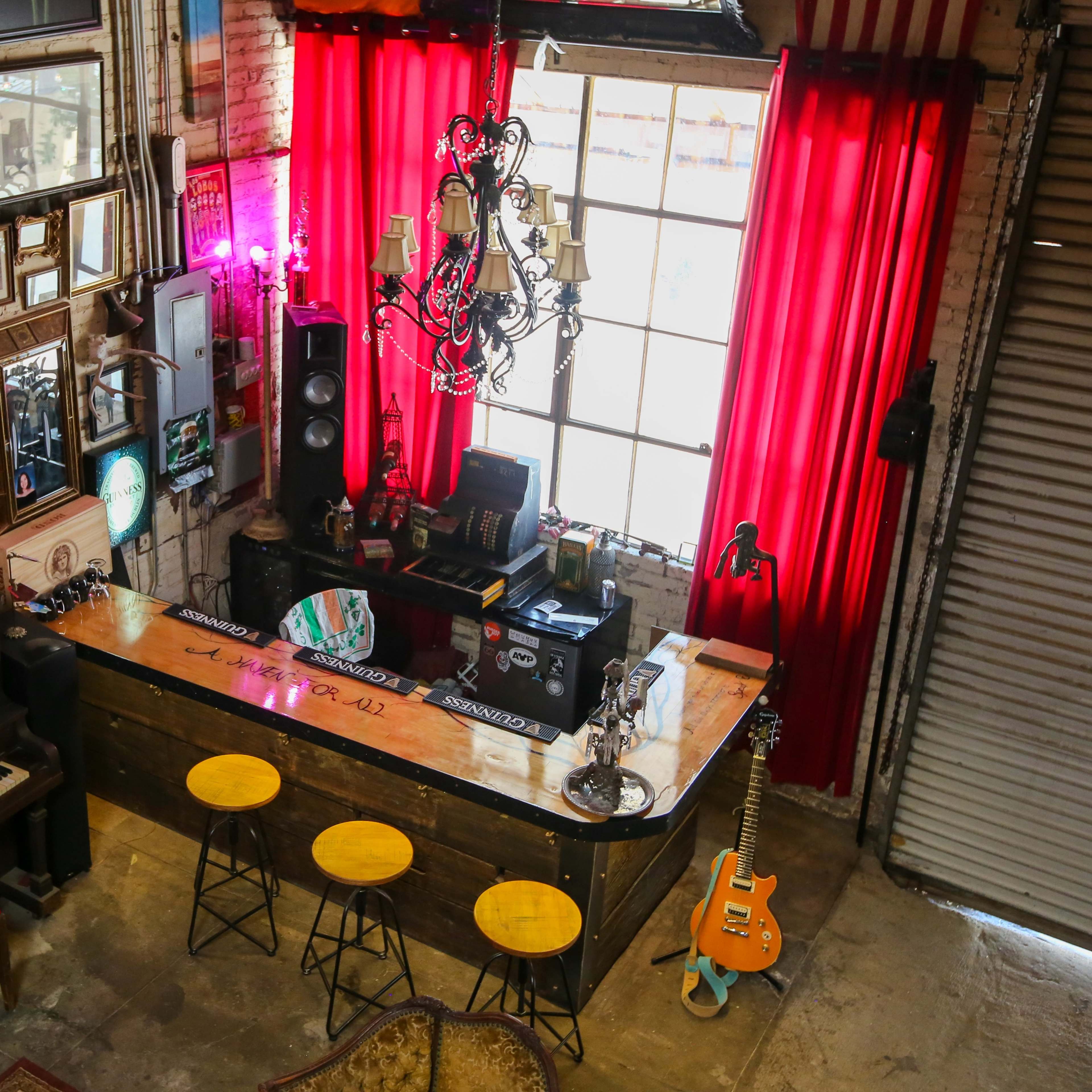 A cozy bar area with a piano, vintage decor on the walls, and a large window draped in red curtains.