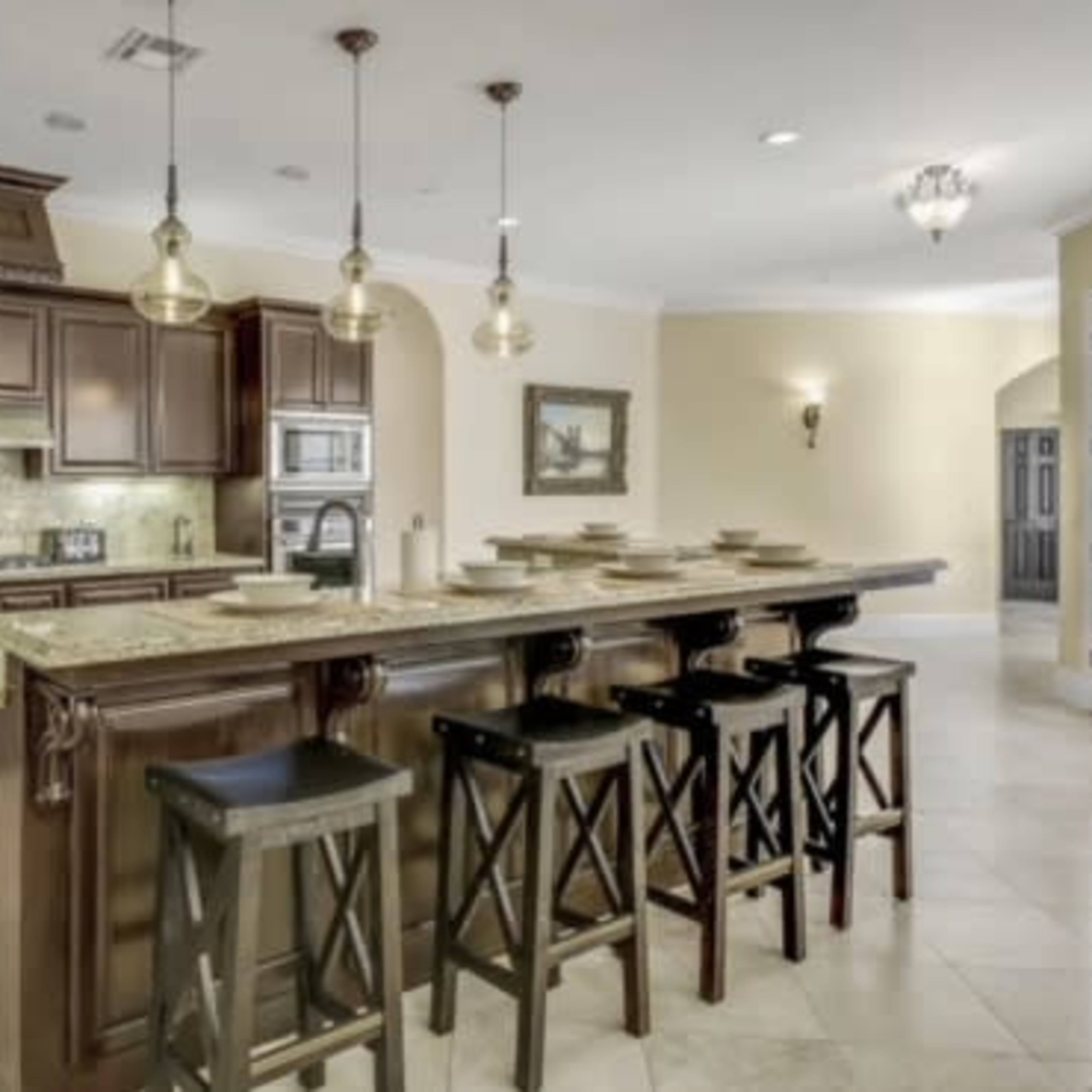 A modern kitchen with dark wooden cabinetry, a large stone island, and several black bar stools.
