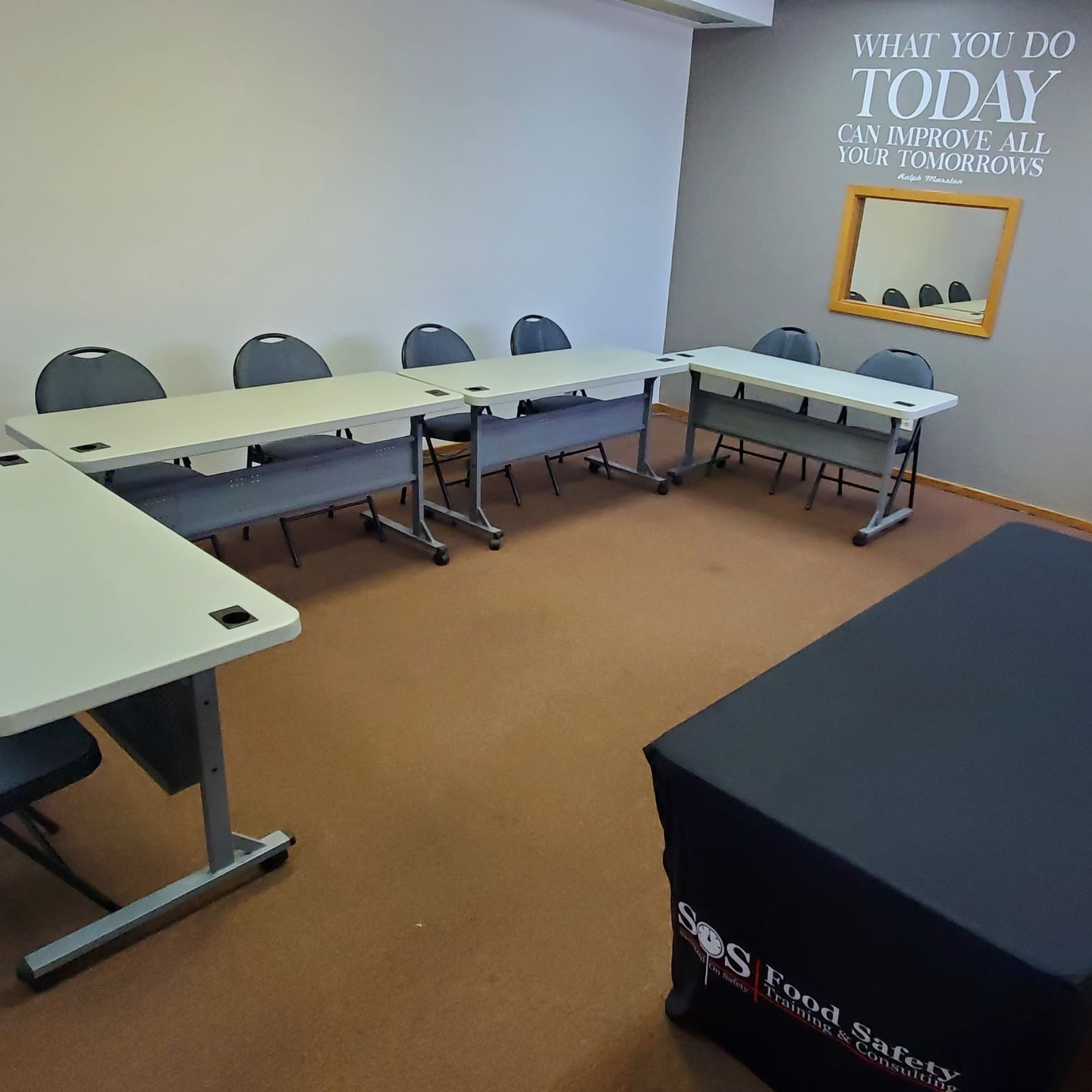 A small meeting room features a U-shaped arrangement of tables and chairs, with a table covered by a black cloth in the foreground.