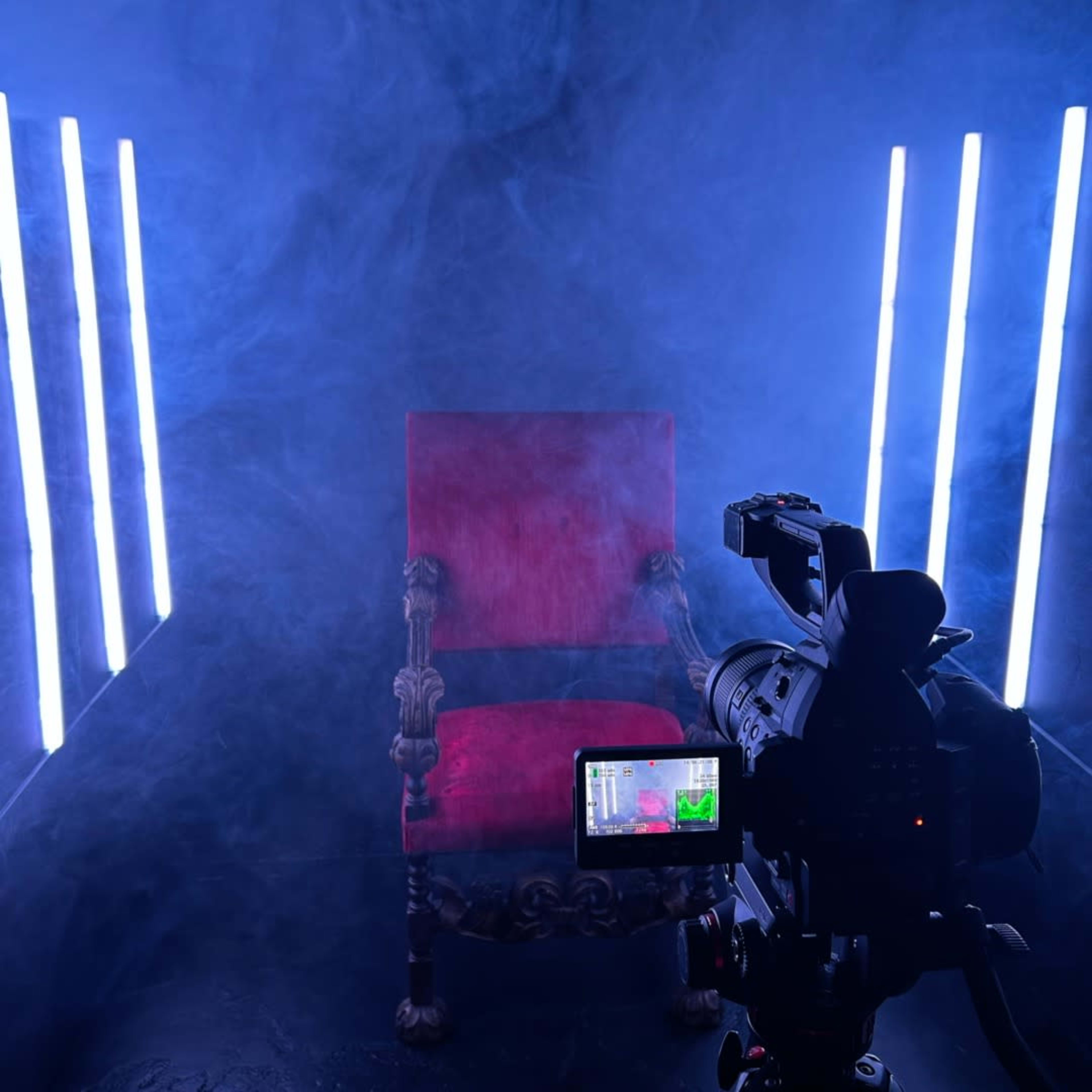 A red chair is positioned in a misty environment, illuminated by vertical neon lights, with a camera recording in the foreground.