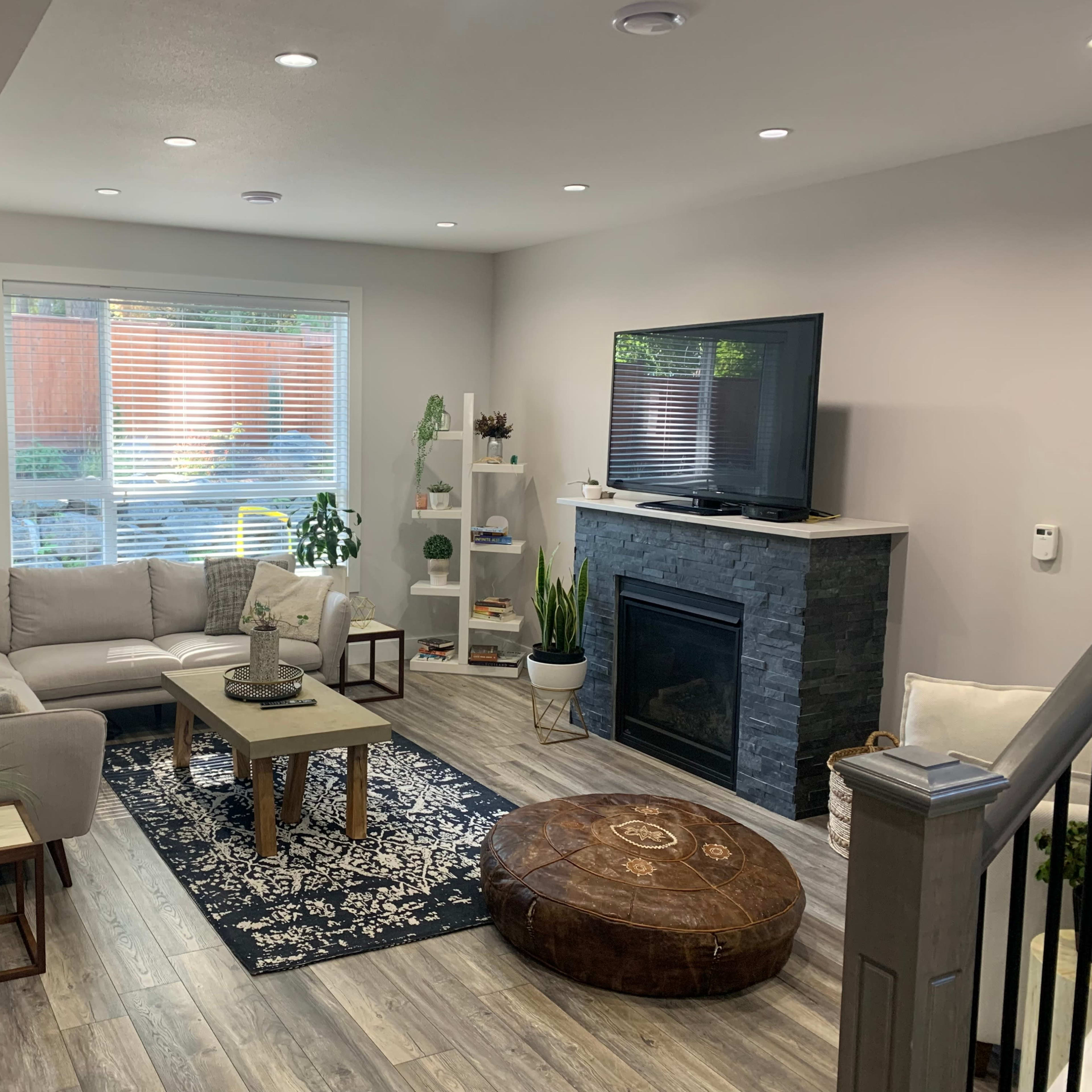 A modern living room with a sectional sofa, a coffee table, a fireplace, a flat-screen TV, and decorative plants.