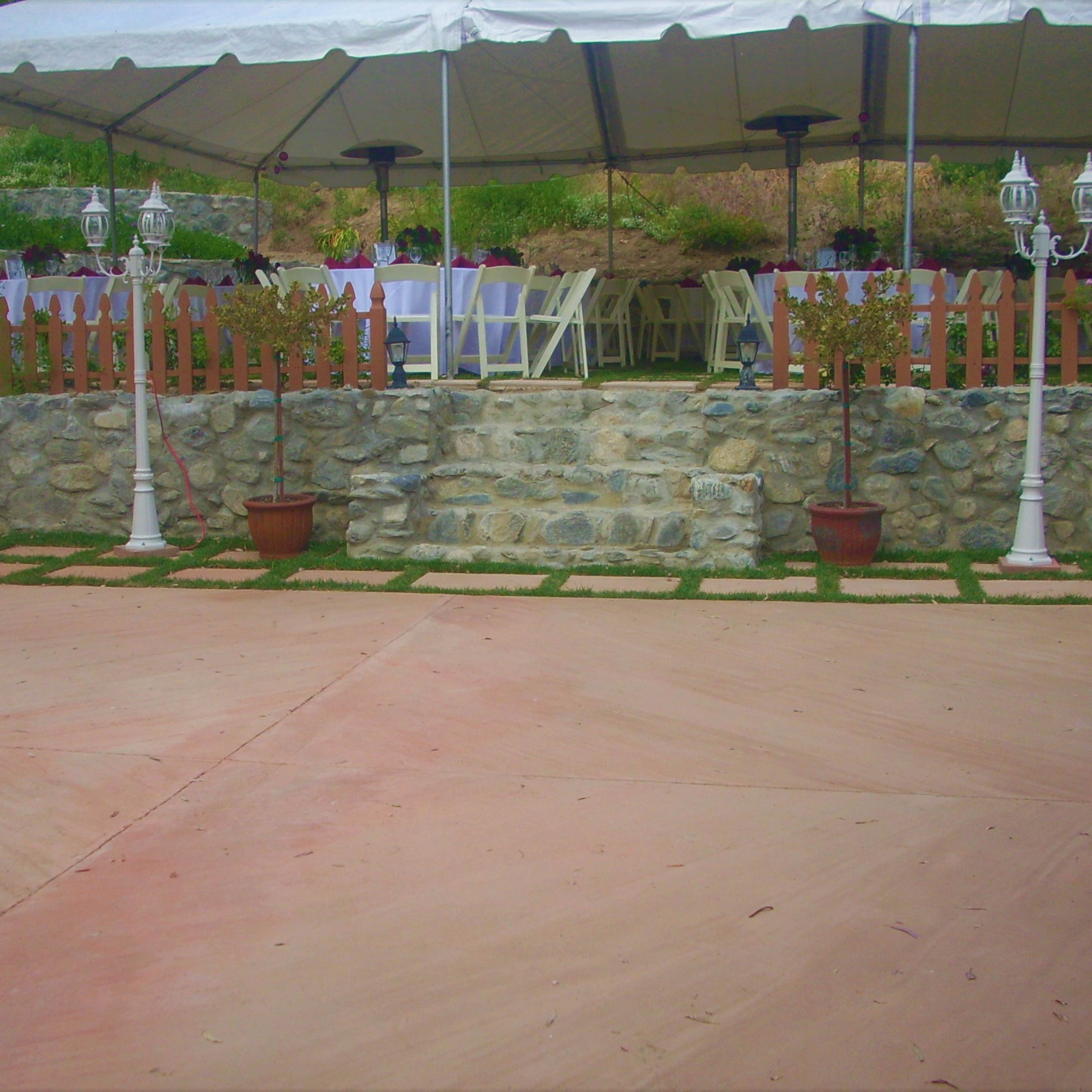 A stone patio area with a tented seating arrangement, surrounded by a landscaped garden and decorative lighting.