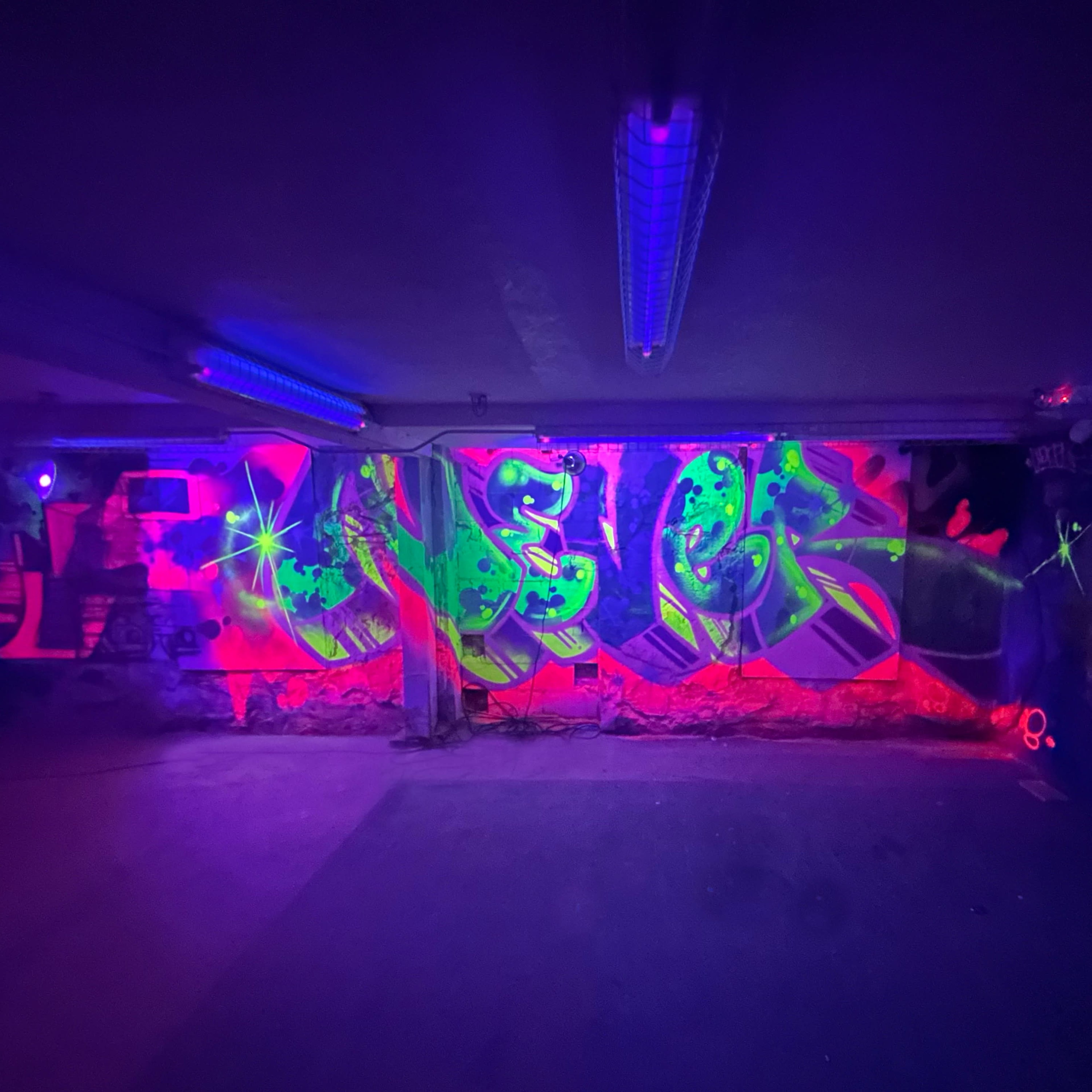 Vibrant graffiti art illuminated by ultraviolet lights in a dimly lit indoor space.