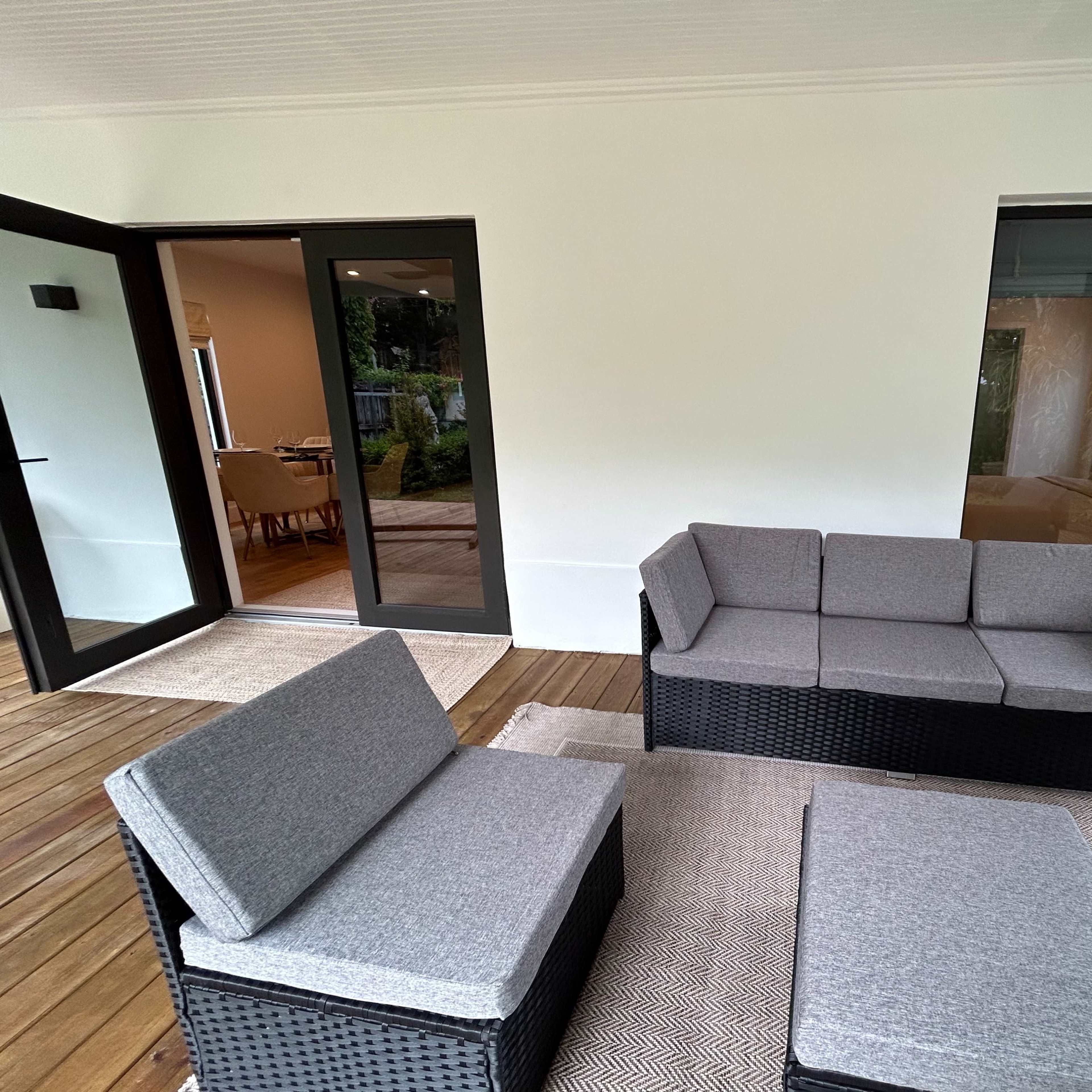 A modern patio area with black wicker furniture and a light-colored rug, leading to large glass doors that open into an interior space.