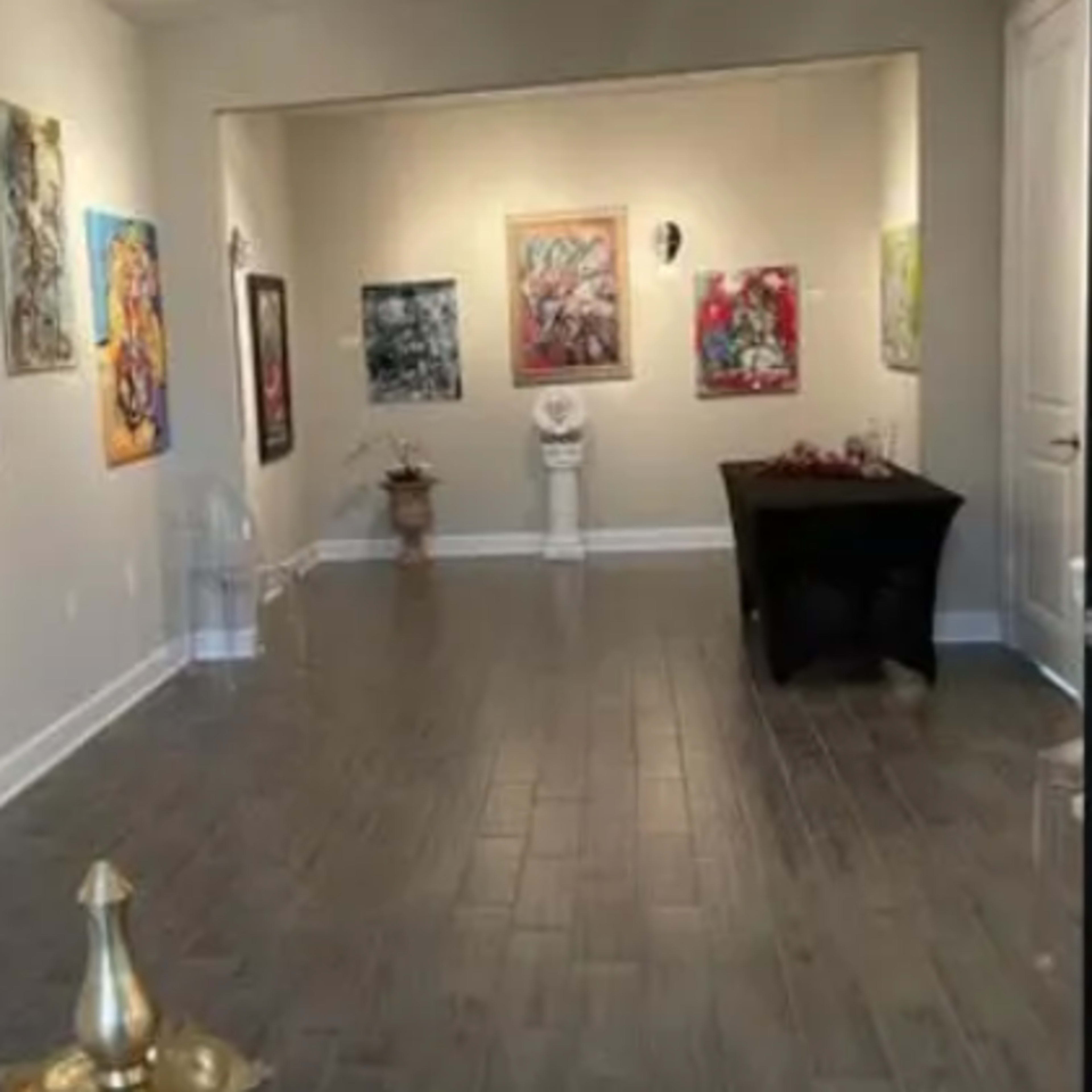 An art gallery with colorful paintings displayed on the walls and a table in the center of the room.