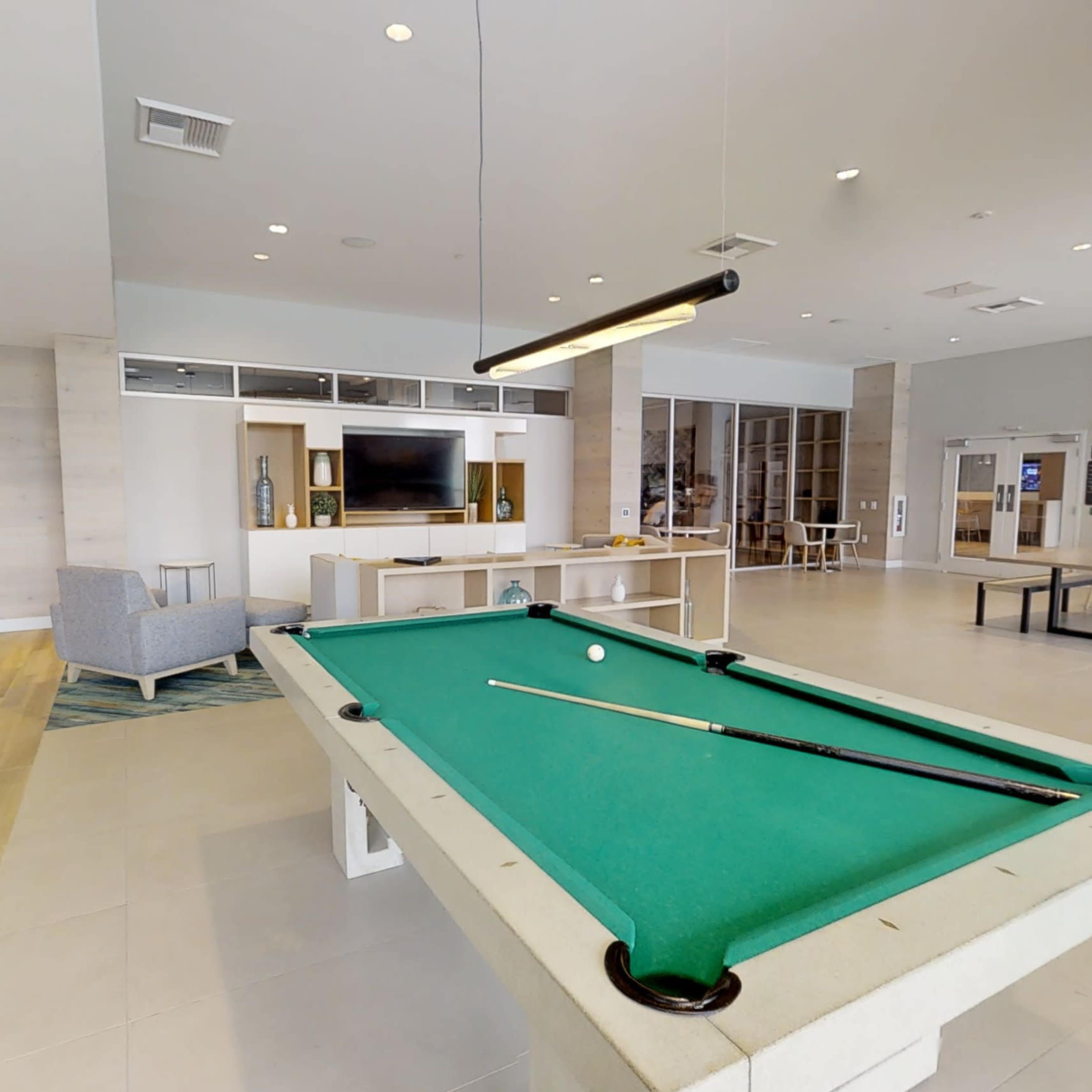 A spacious lounge area featuring a green pool table, seating arrangements, and a large wall-mounted TV.