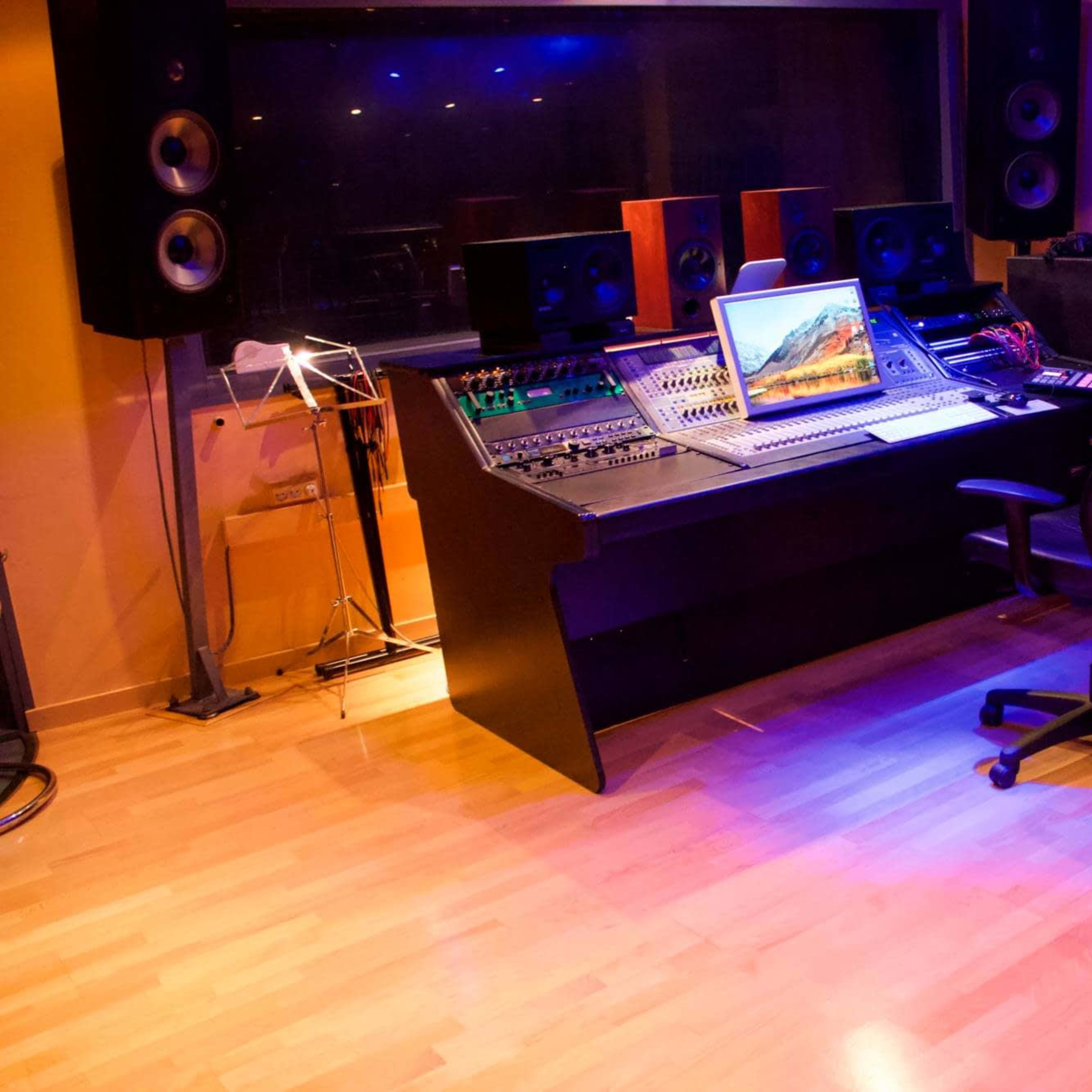 A recording studio with a mixing console, computer, keyboard, and speakers, all arranged in a well-lit space with wooden floors.