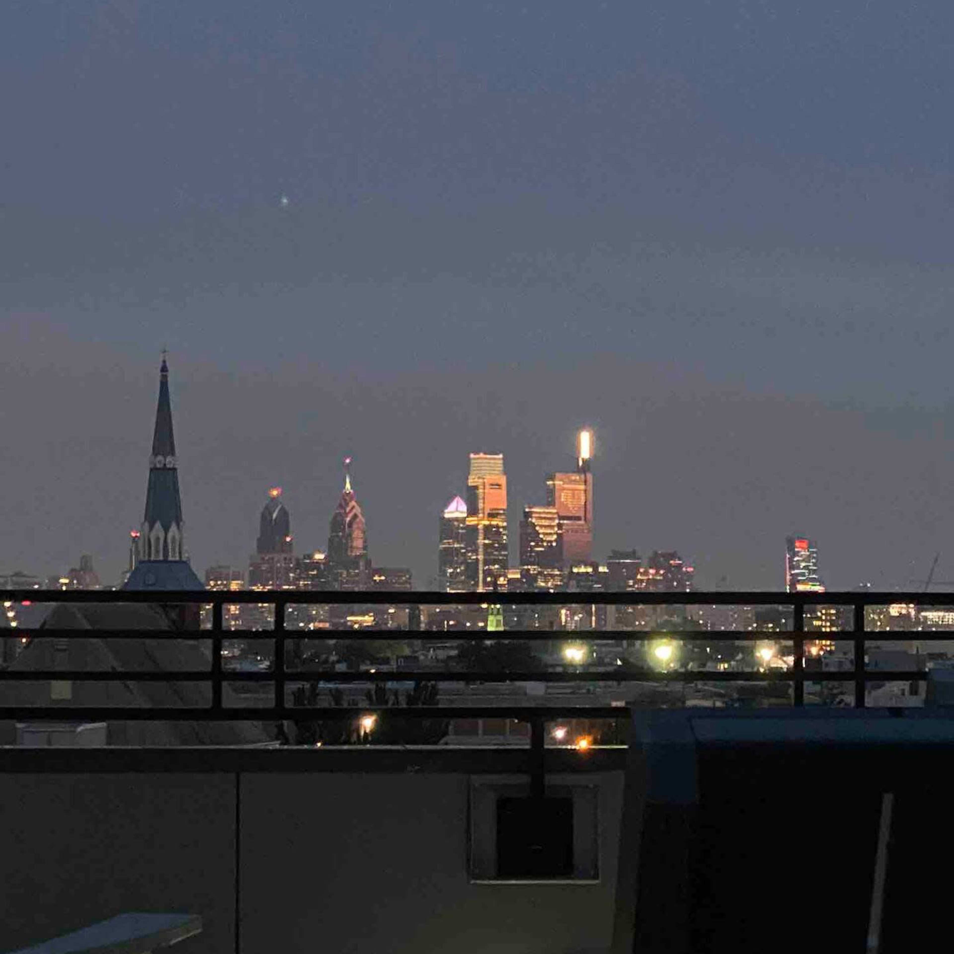 A nighttime view of the Philadelphia skyline with several illuminated buildings and a church steeple in the foreground.