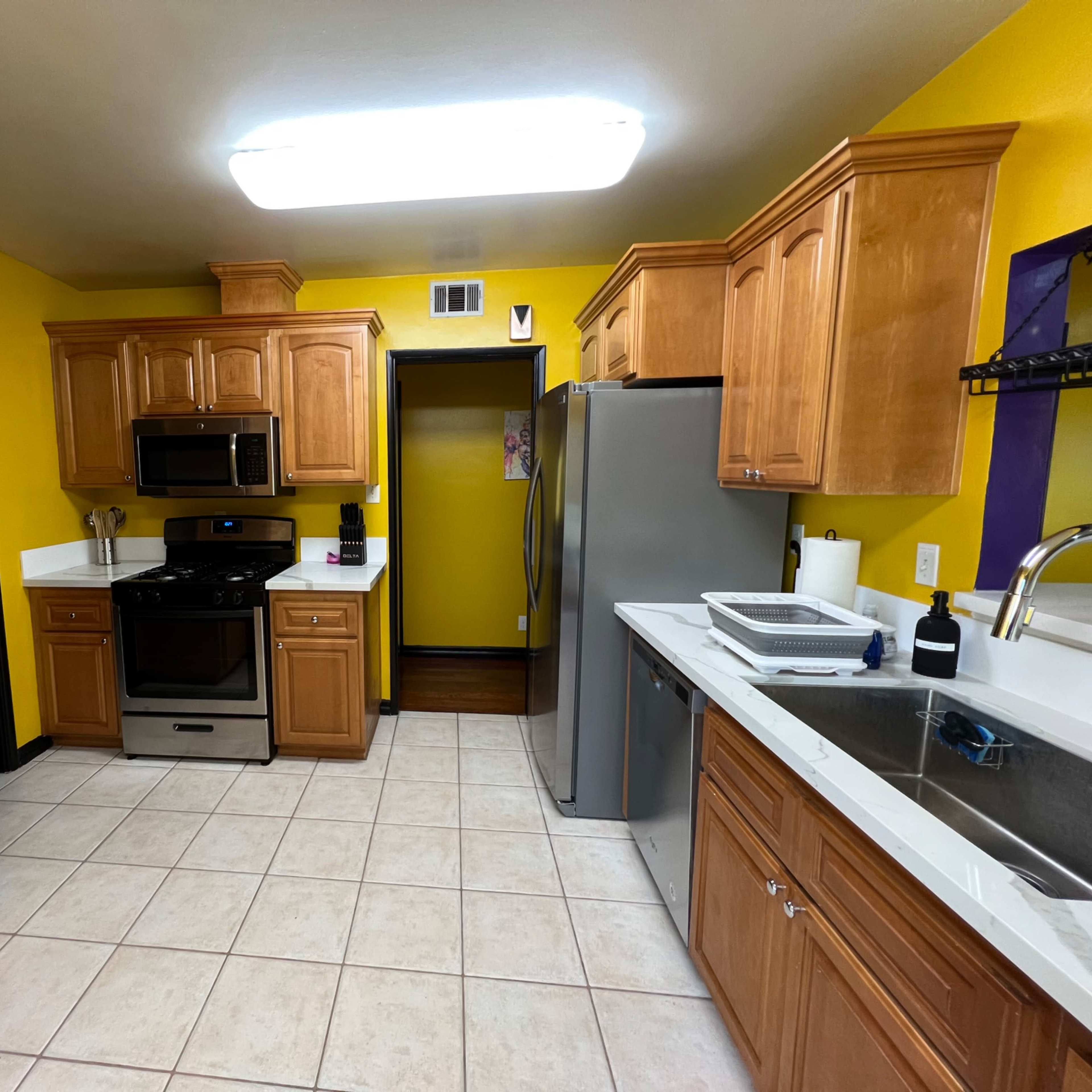 The kitchen features wooden cabinetry, stainless steel appliances, and yellow walls, with a tiled floor.
