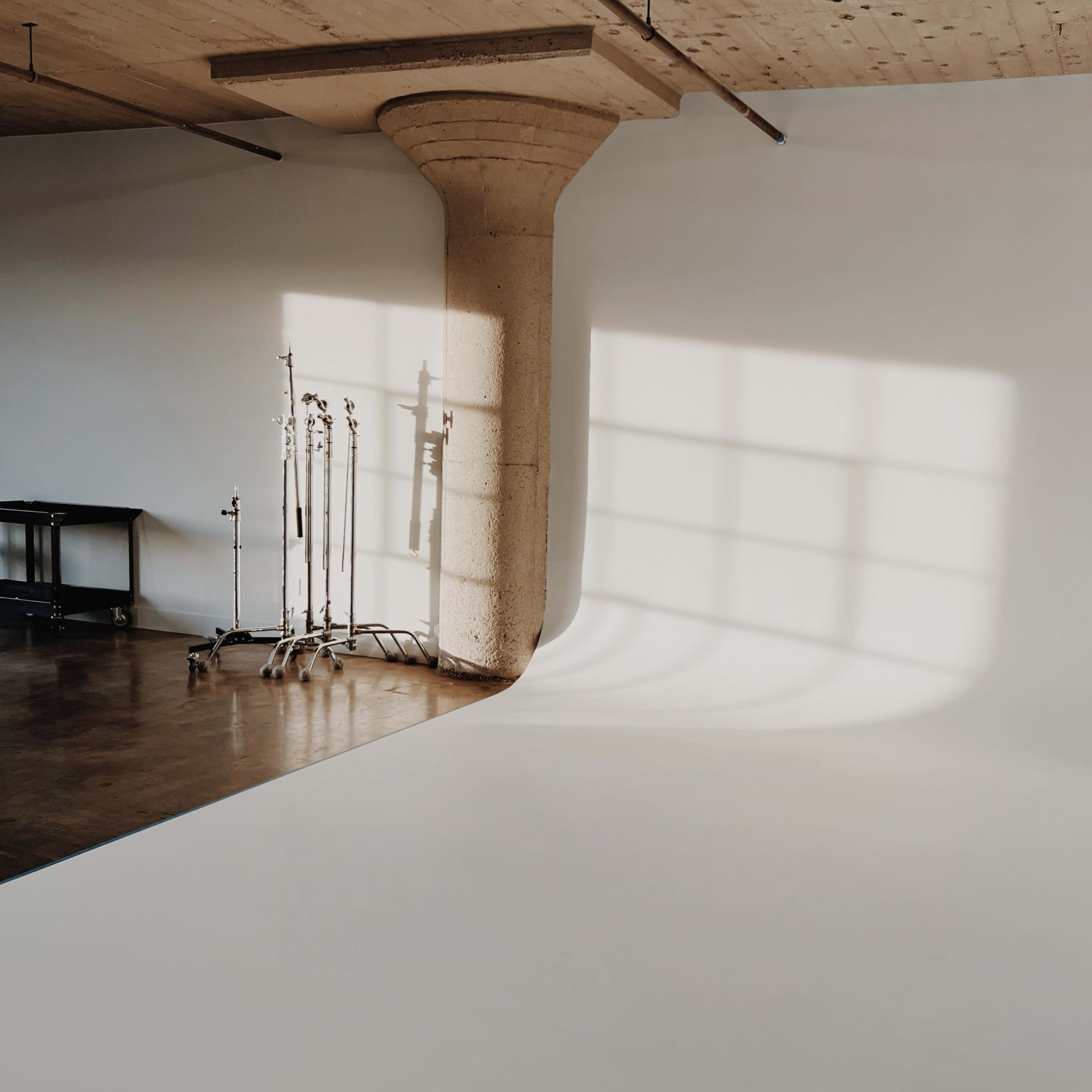 A minimalistic photography studio with a curved white backdrop and a concrete support pillar, illuminated by soft natural light.